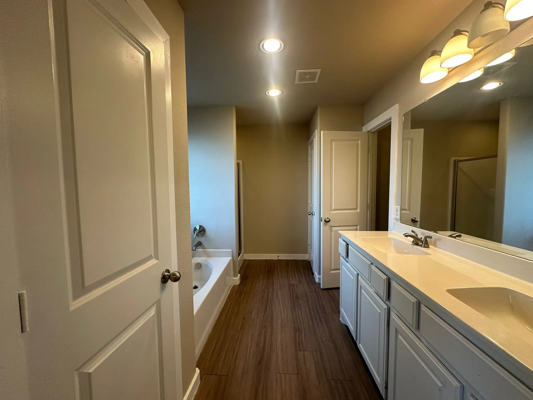 Bathroom featuring a double vanity with integrated sinks, wood-finish flooring, recessed lighting, and a bathtub with a shower head
