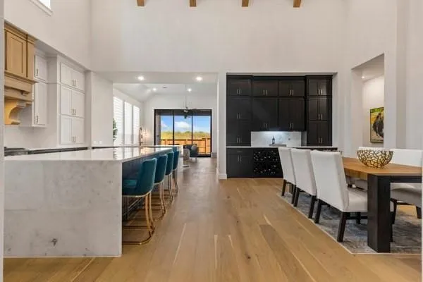 Open-concept kitchen and dining area featuring a large center island with waterfall countertop, extensive cabinetry, light wood-finish flooring, and exposed ceiling beams