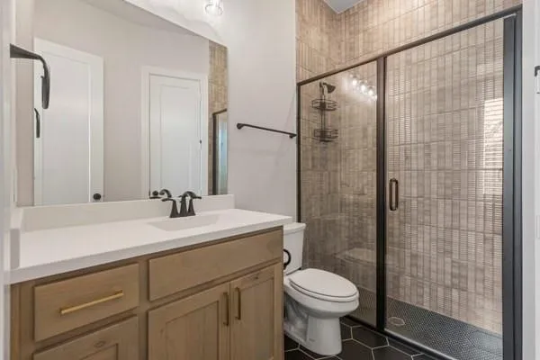 Vanity with a light-toned wood-finish cabinet and white countertop, black matte faucet, framed mirror, and a walk-in shower with textured tile and dark-framed glass doors