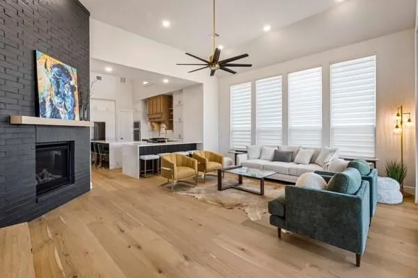 Open-concept living space featuring wood-finish flooring, a contemporary fireplace with a dark brick surround, and multiple tall windows