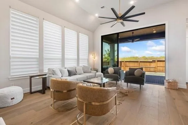 Vaulted ceiling with an installed ceiling fan, light wood-finish flooring, multiple windows with installed window treatments, and a large sliding glass door