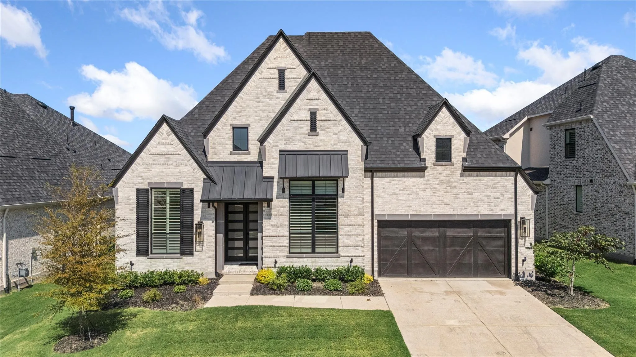 Light-colored brick exterior with dark shingle roof, contrasting dark shutters, and a prominent front-facing garage