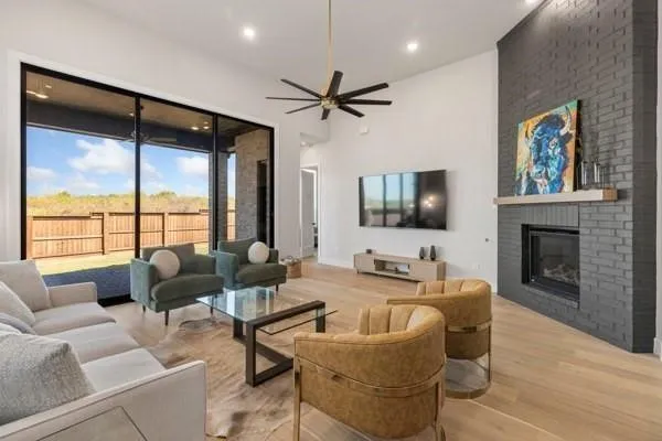 Vaulted ceilings, a dark brick fireplace, a wood mantel, a ceiling fan, and sliding glass doors