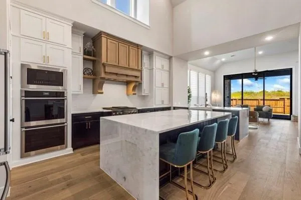 Kitchen featuring wood-finish flooring, two large kitchen islands with waterfall countertops, stainless steel double oven, and a built-in microwave