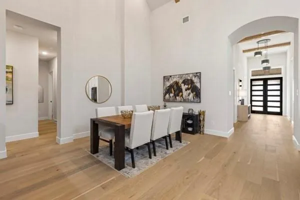 High ceilings, light wood-finish flooring, arched entryway, modern pendant lighting, and a double-panel entry door