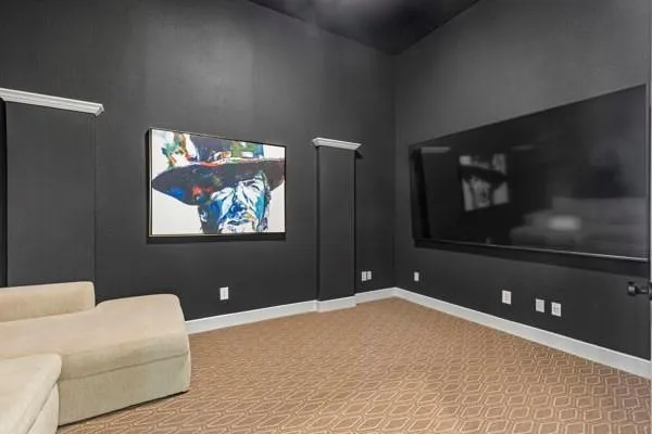 Media room featuring dark wall paint, patterned carpet flooring, white baseboards, and a large wall-mounted screen