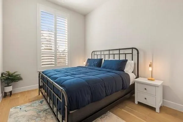 Wood-finish flooring, white walls, and a tall window with louvered shutters