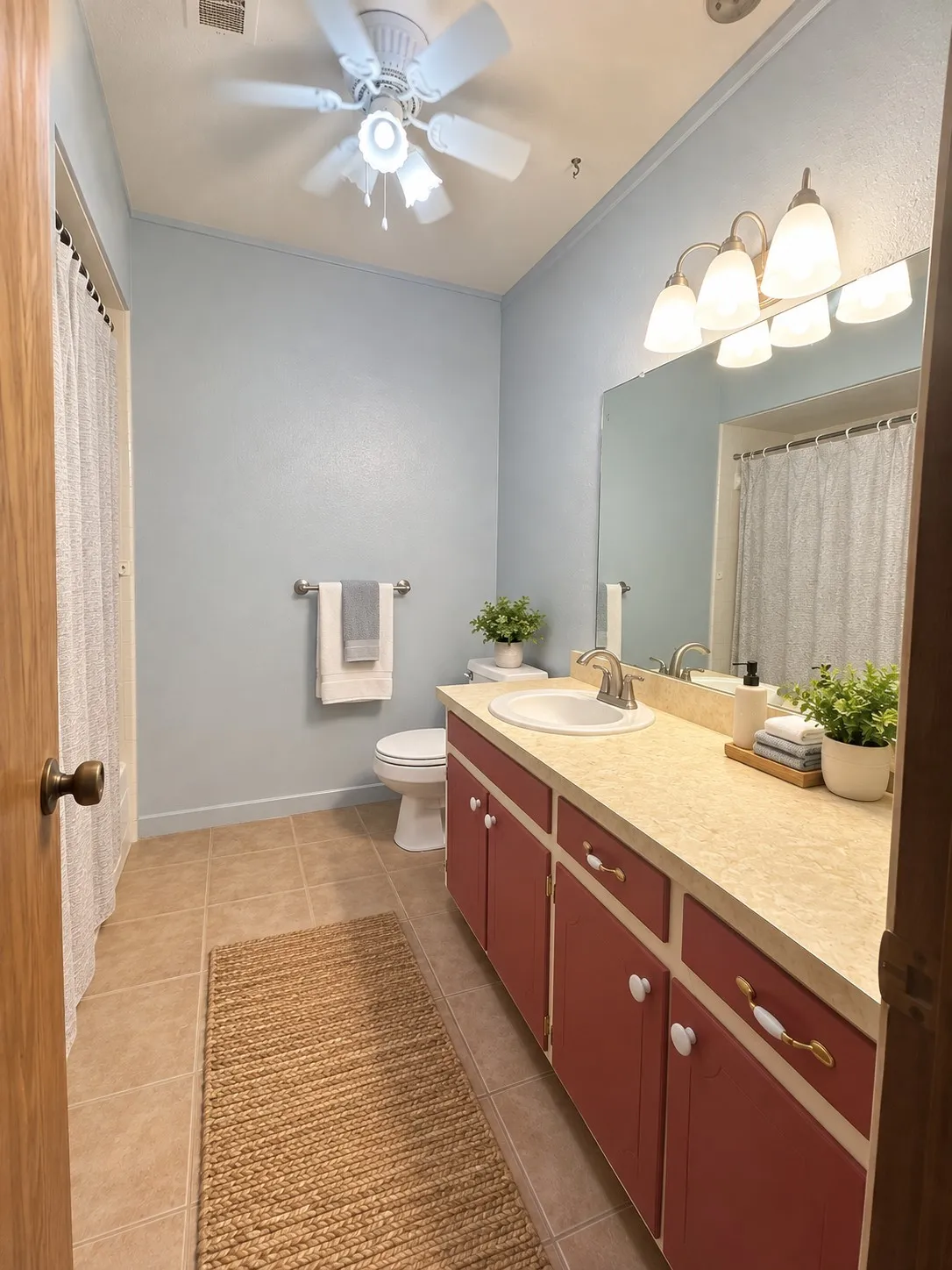 Bathroom featuring a single vanity with a laminate countertop, red cabinetry, and a ceiling fan