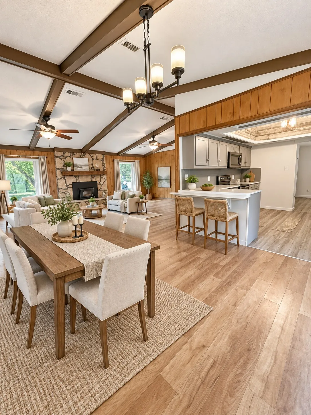 Vaulted ceiling with exposed wood beams, wood-finish flooring, stone-clad fireplace, and kitchen with breakfast bar