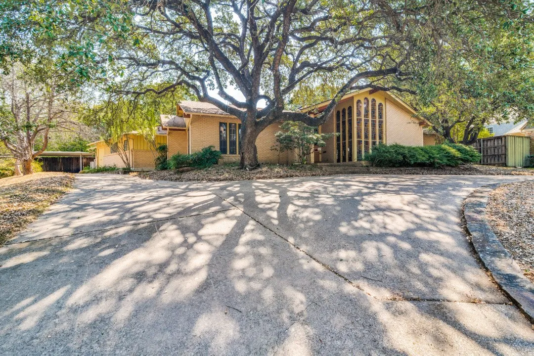 Brick exterior with mature trees, a multi-pane arched window, and a concrete drive