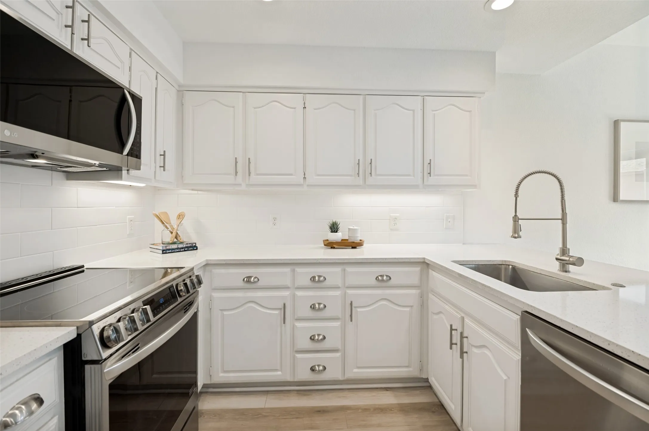 Crisp white cabinetry is paired with gleaming quartz countertops, a classic subway tile backsplash, and stainless steel appliances, including a built-in microwave, dishwasher, and range, creating a bright and inviting space. The oversized farmhouse sink and sleek gooseneck faucet add both elegance and functionality, while under-cabinet lighting enhances the clean, sophisticated design.