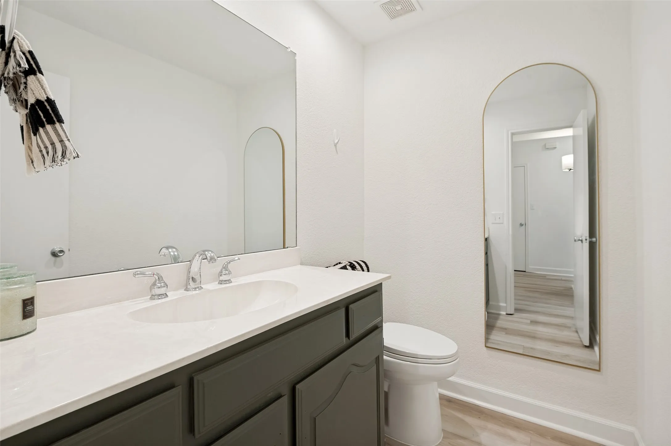 This stylish guest half bath has been thoughtfully updated with a clean, modern aesthetic. A spacious vanity with ample counter space and storage is complemented by a large mirror that enhances the bright and open feel of the room. Fresh finishes, updated flooring, and neutral tones create a timeless look that blends seamlessly with the home's overall design. Conveniently located for guests, this powder bath offers both comfort and functionality while providing an elegant space for visitors.