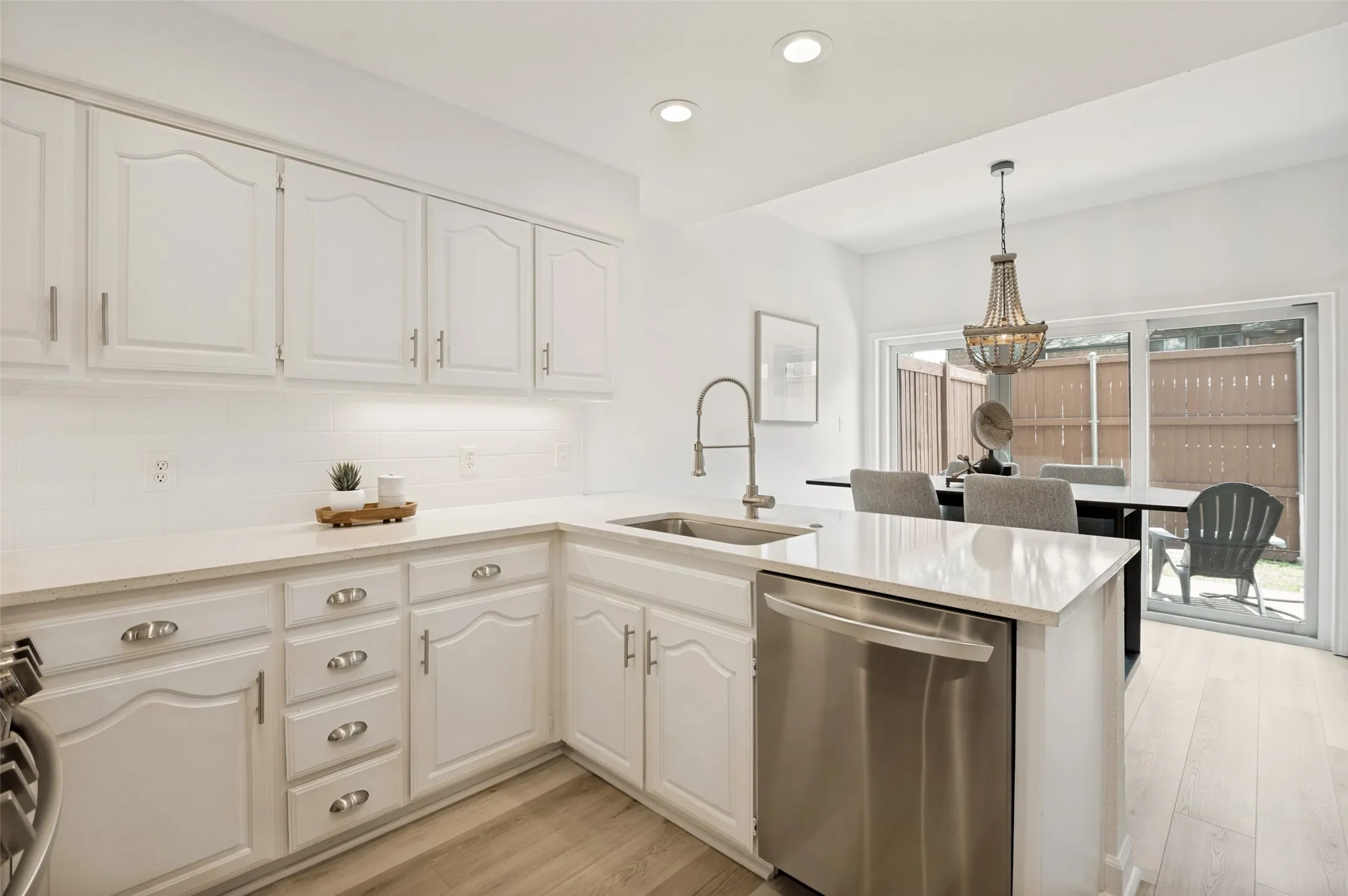 This bright and inviting kitchen showcases a clean and timeless design. Light wood-look luxury vinyl flooring flows seamlessly through the kitchen into the adjacent dining area, creating a warm, cohesive feel throughout the home.