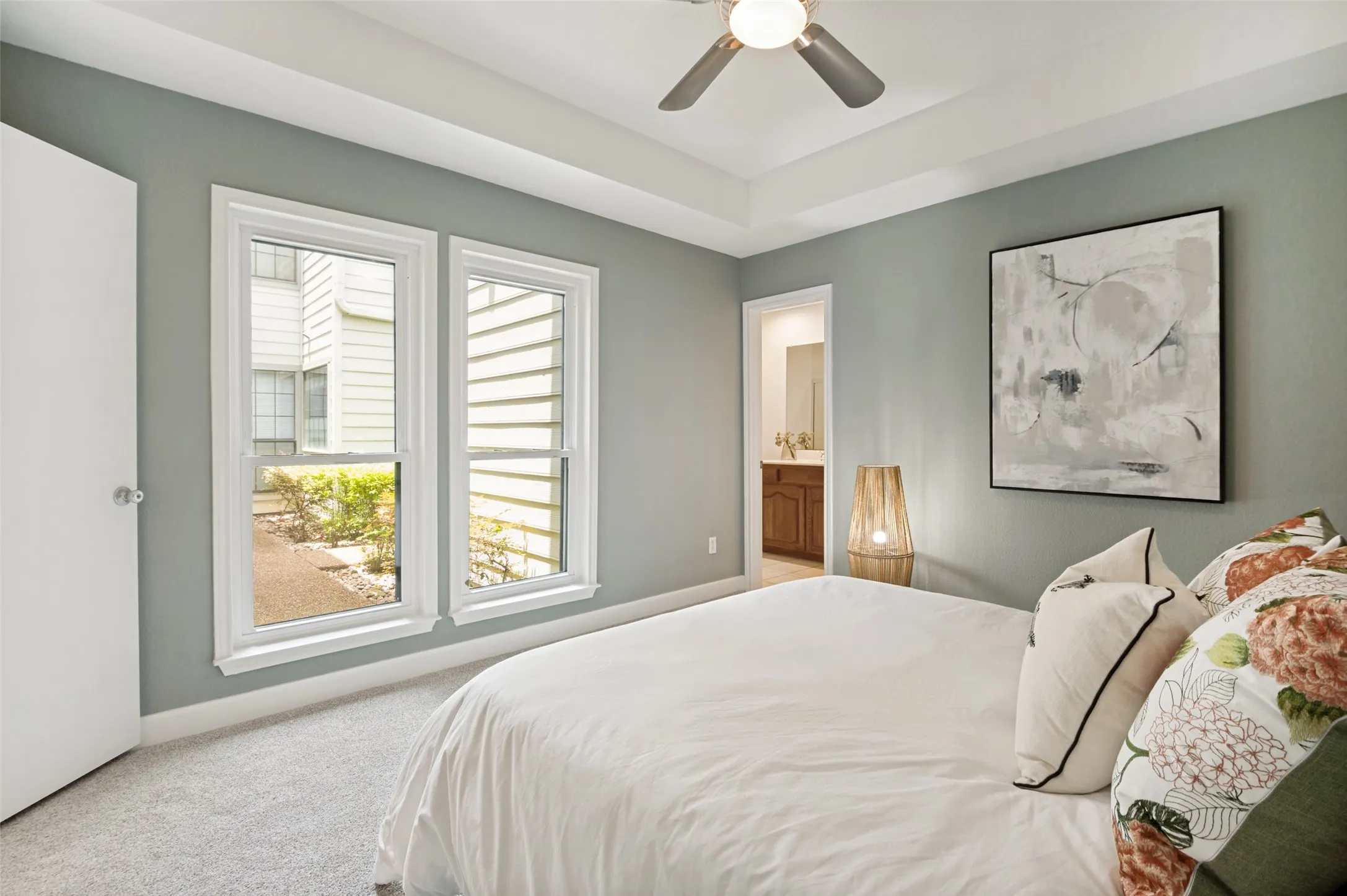 A tray ceiling adds architectural elegance and enhances the room’s airy feel, while large windows invite natural light and create a bright, welcoming atmosphere. Soft neutral tones and plush carpeting and a ceiling fan provide warmth and comfort, making this the perfect place to relax and recharge.