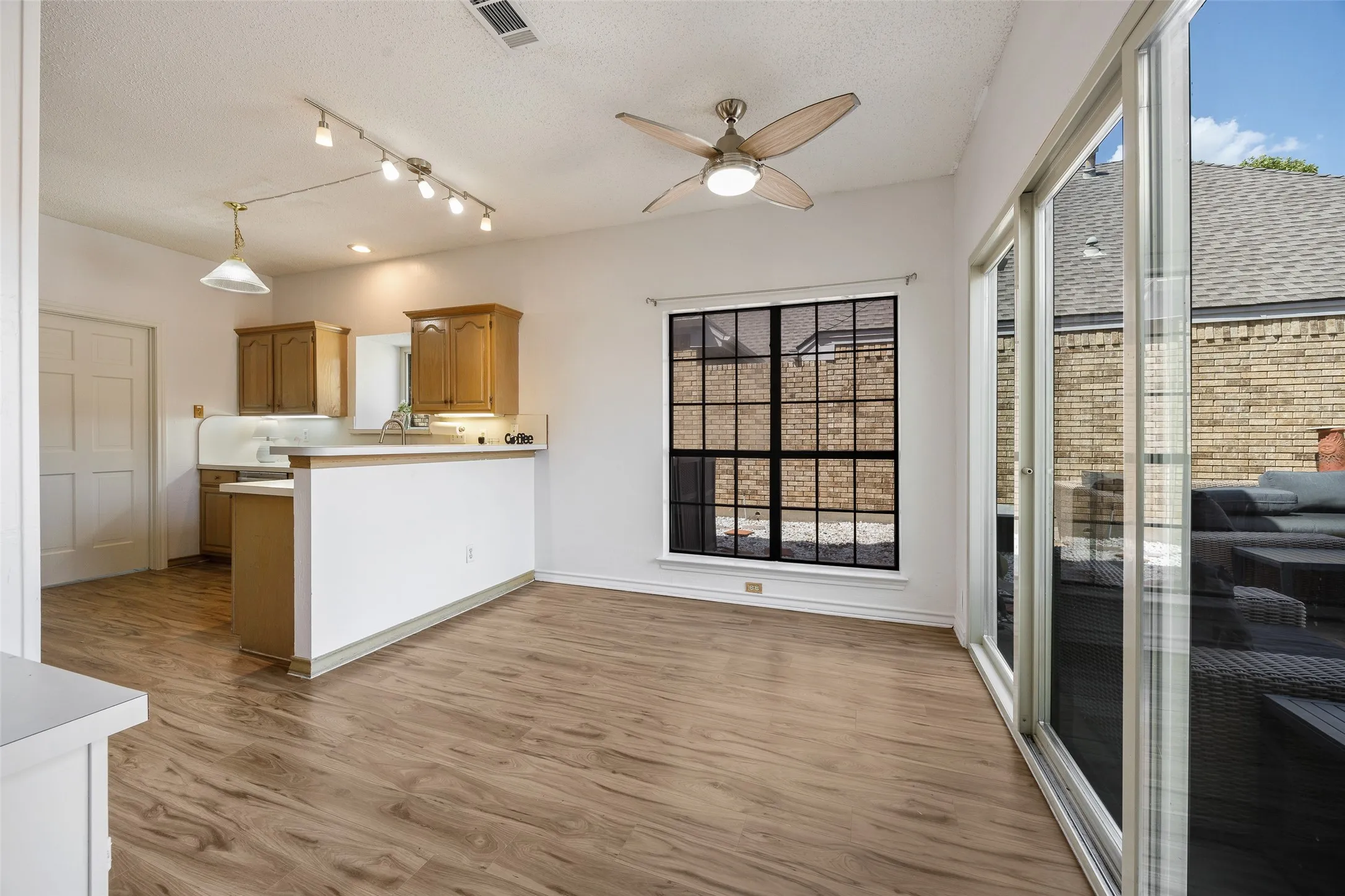 Open-concept living space featuring wood-finish flooring, a ceiling fan with integrated lighting, and track lighting