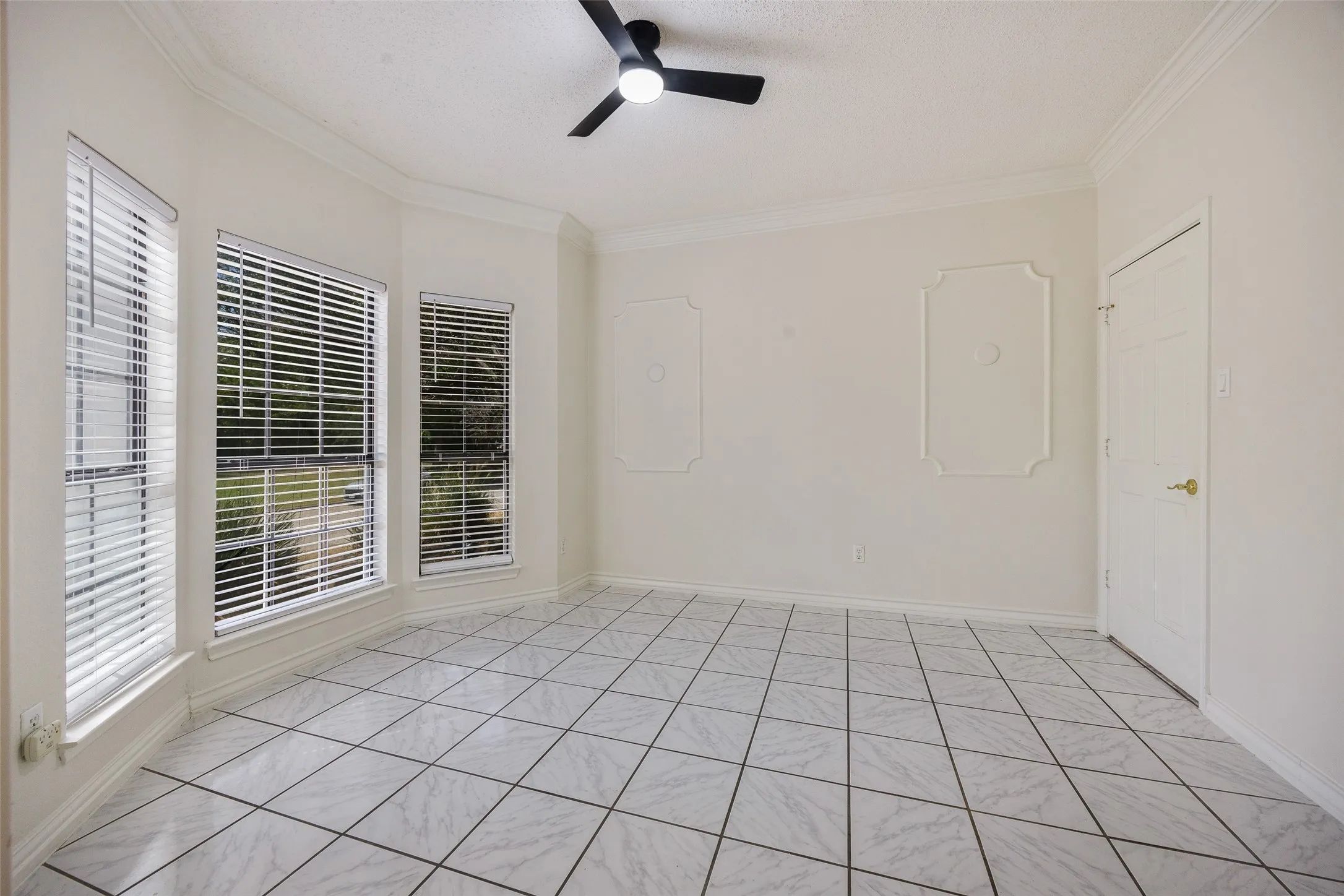 White tile flooring, three large windows with blinds, crown molding, a ceiling fan, and decorative wall molding
