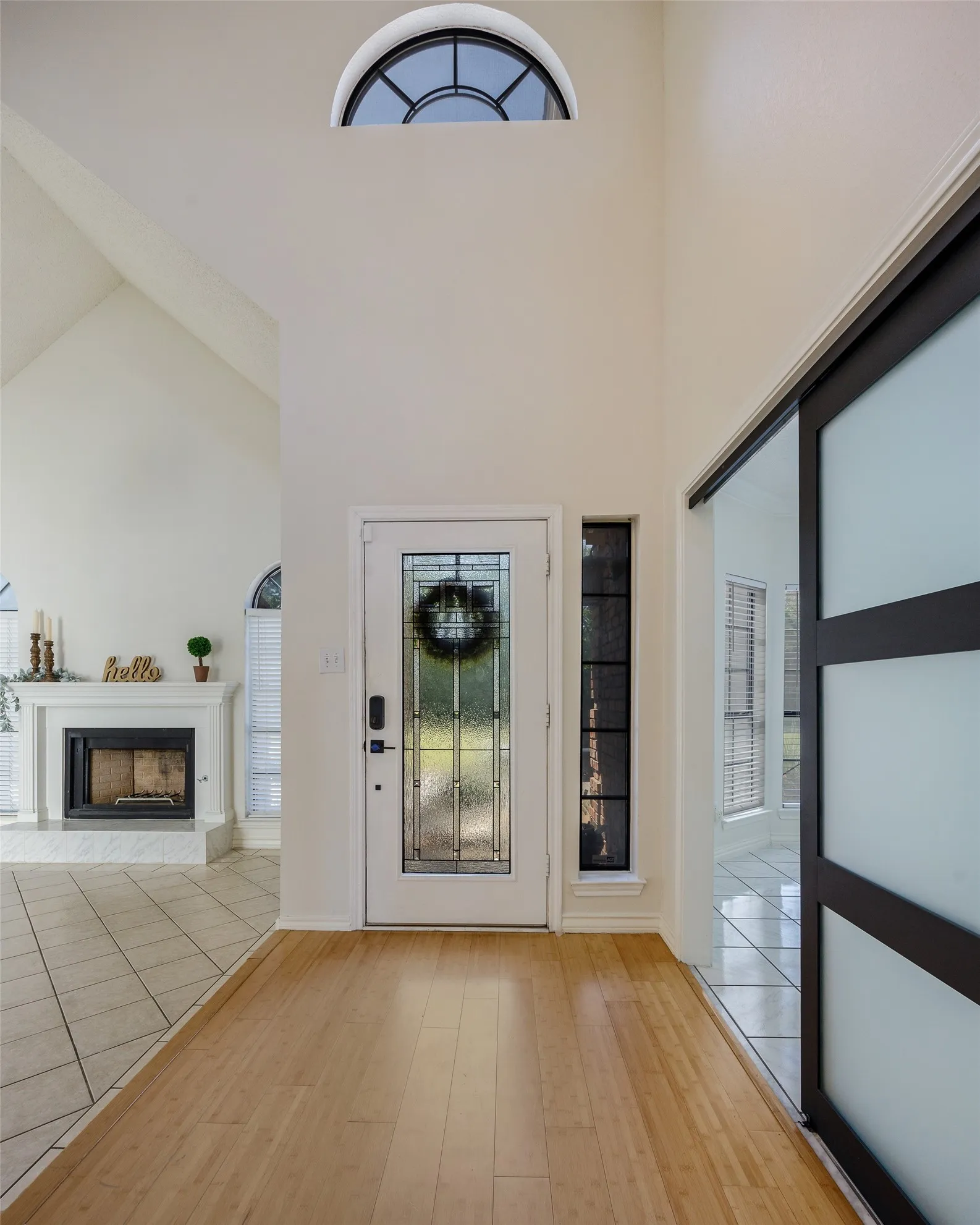 Arched transom window, wood-finish flooring, white door with decorative glass, side light window, and barn door with frosted panels