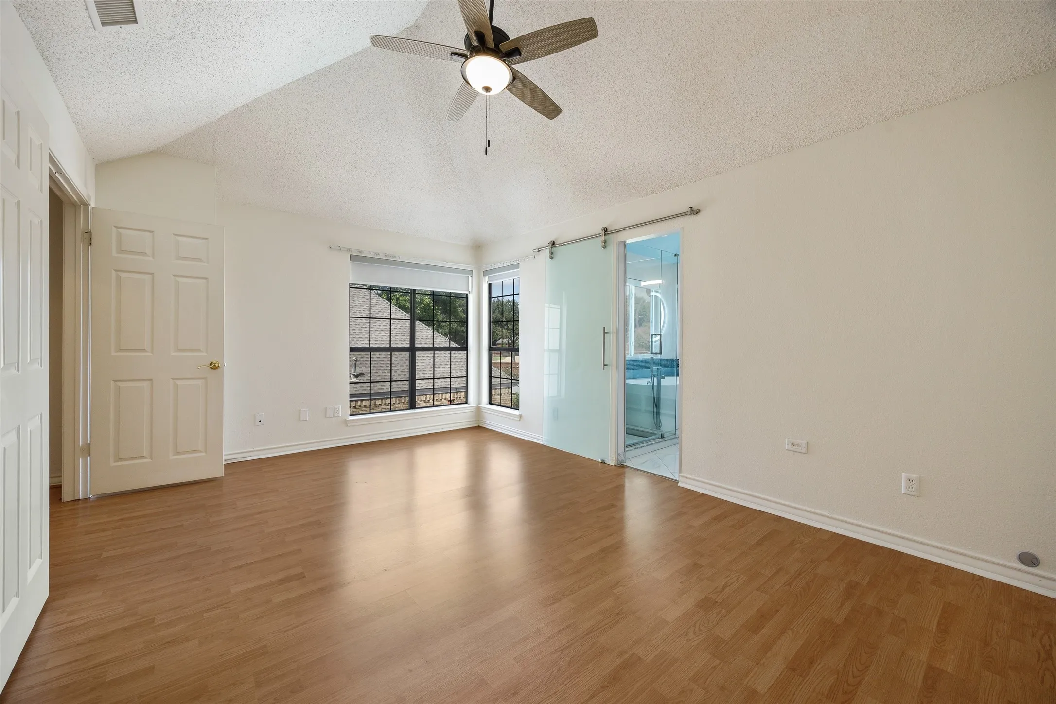 Vaulted ceiling with a ceiling fan, wood-finish flooring, multiple windows, and a frosted glass barn door