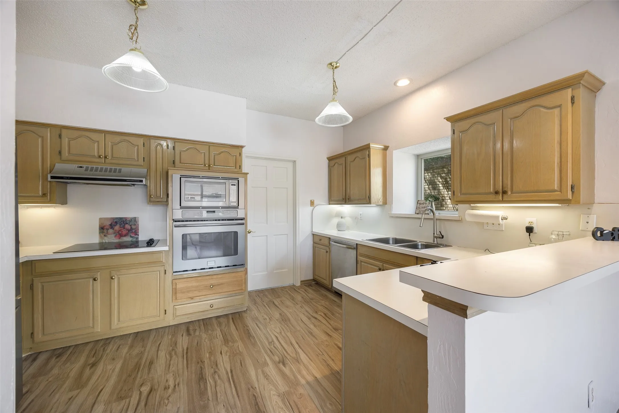 Wood-finish flooring, built-in stainless steel appliances, dual basin sink, light wood cabinetry, and recessed lighting