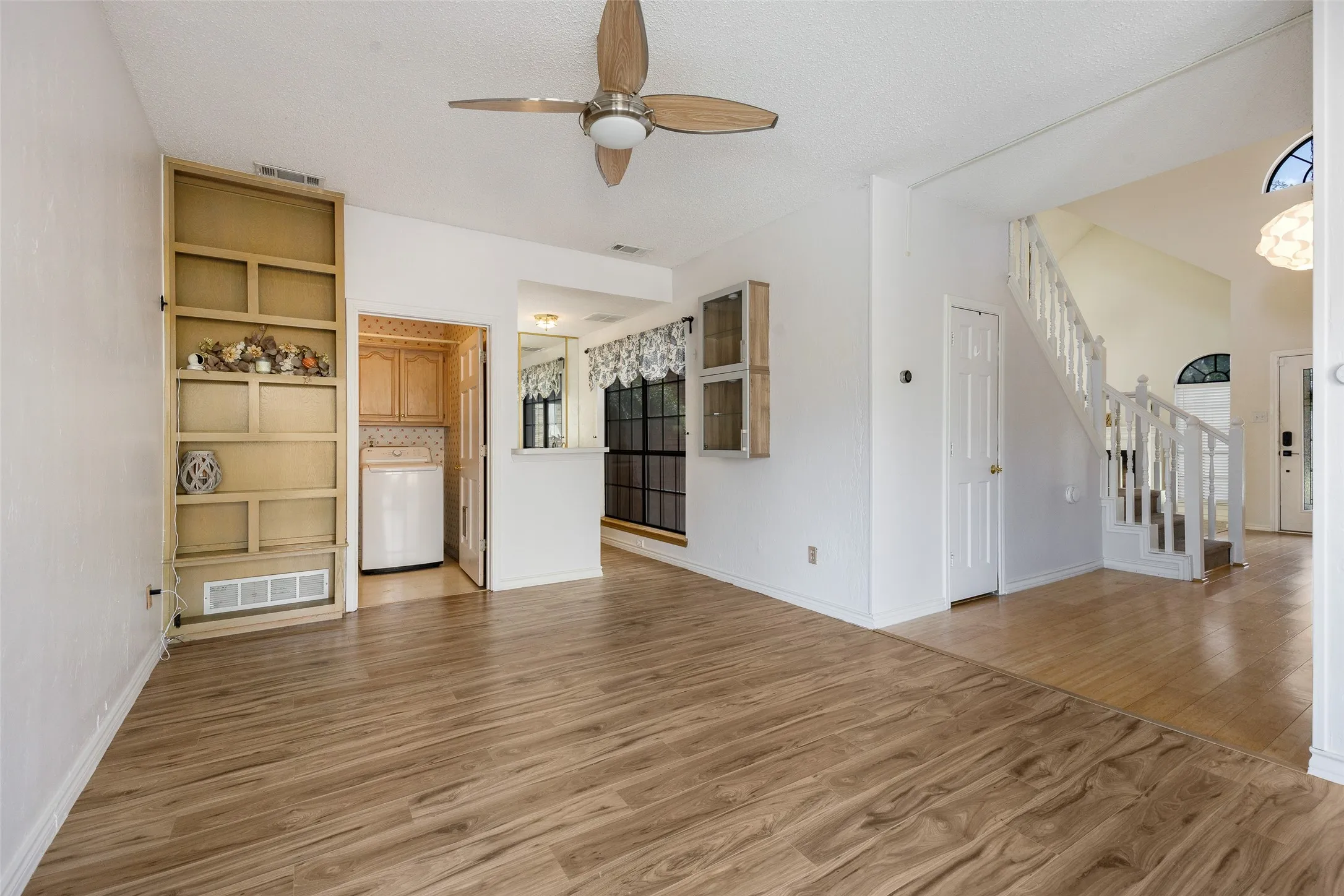 Wood-finish flooring, built-in shelving, ceiling fan, and staircase with white railings