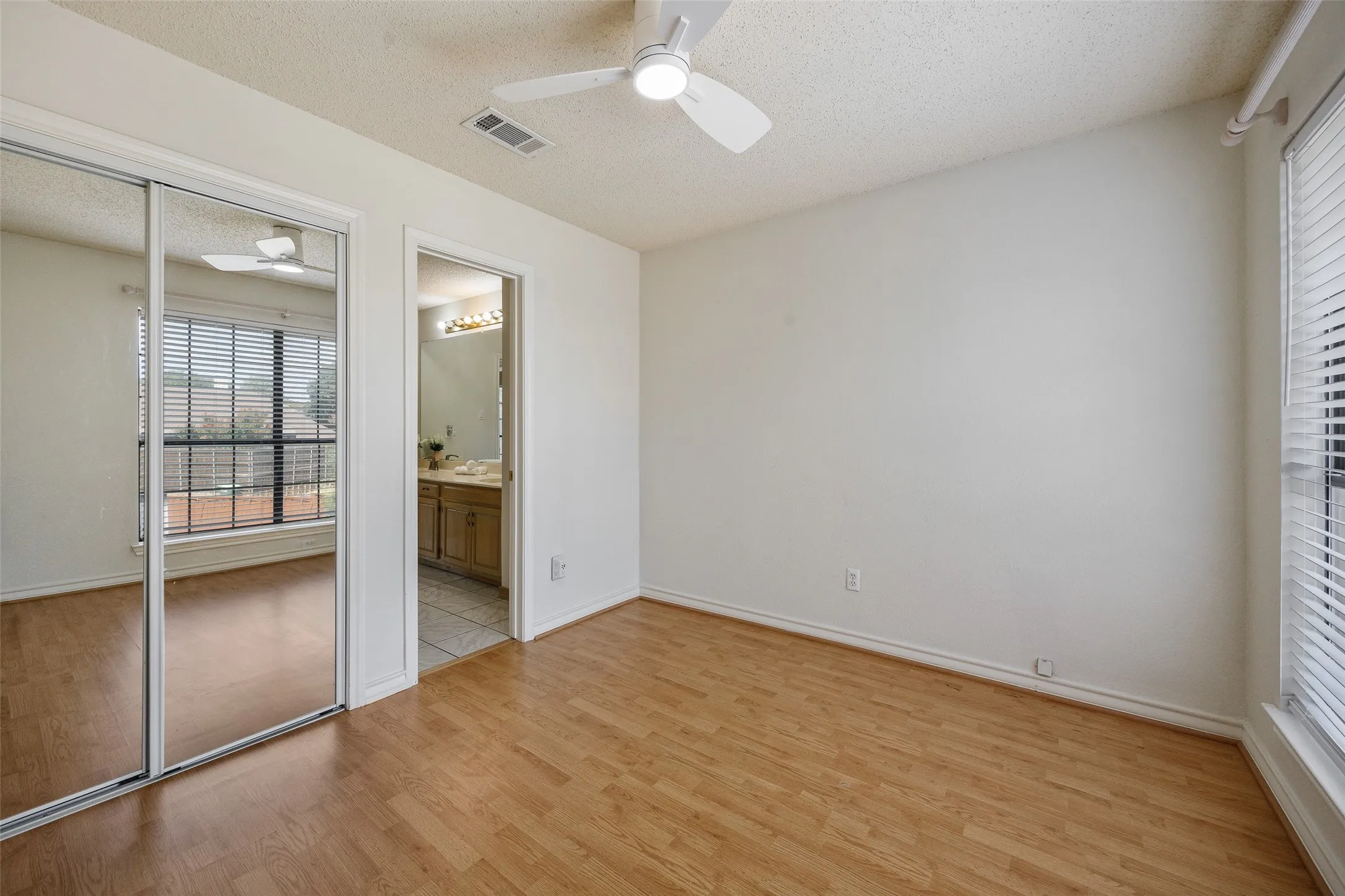Wood-finish flooring, mirrored sliding closet doors, ceiling fan, and a large window with blinds