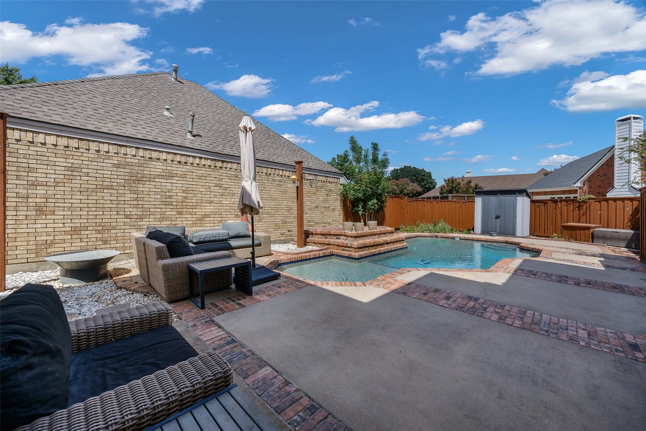 Backyard featuring a built-in swimming pool, integrated spa, and concrete patio with brick accents
