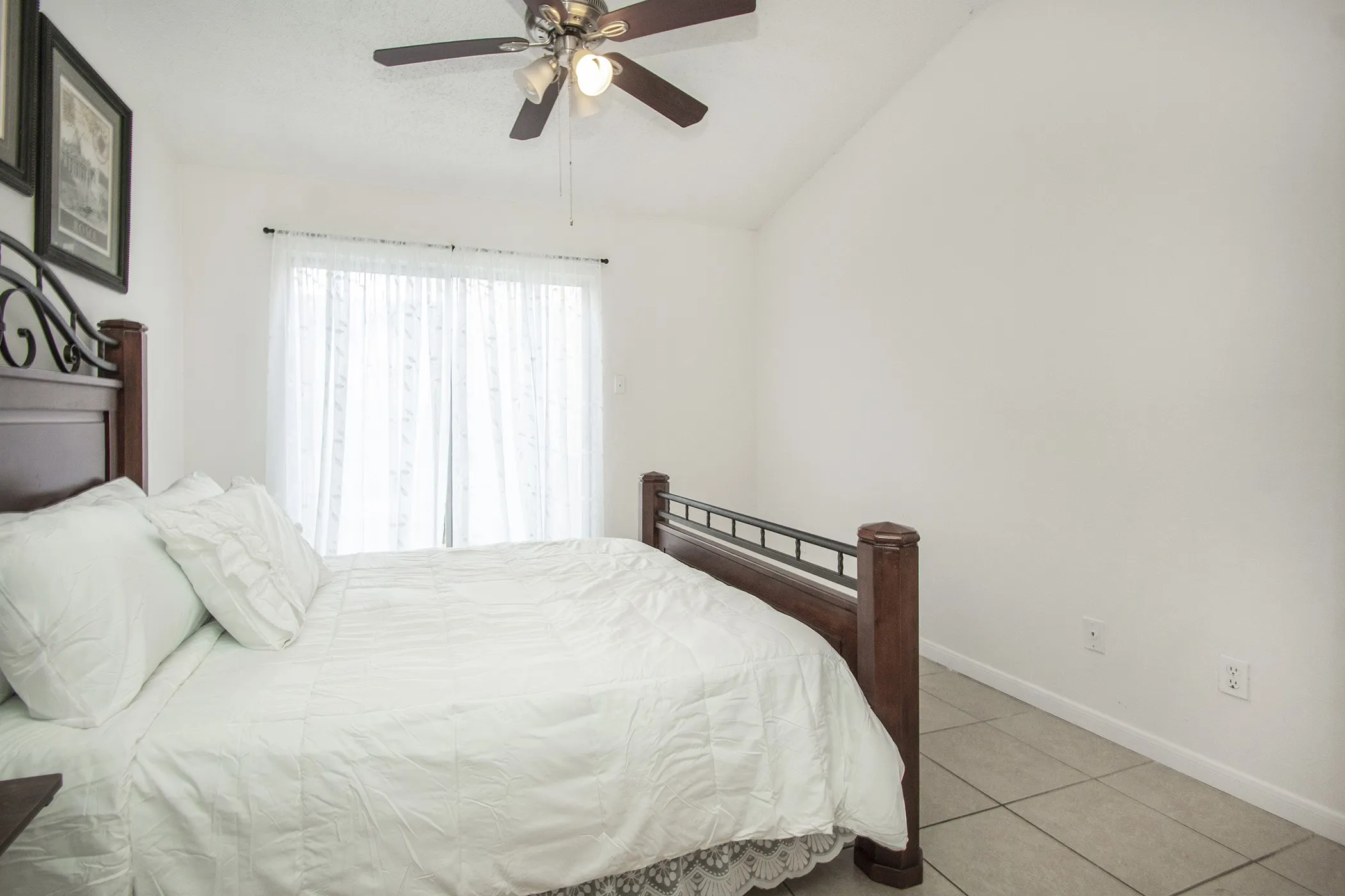 Vaulted ceiling, ceiling fan with integrated lighting, sliding glass door, tiled flooring, neutral wall color