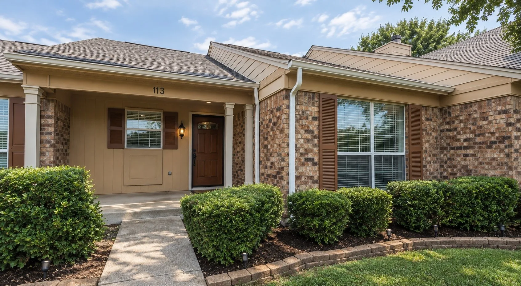 Brick veneer facade with shuttered windows, a covered front entry, and a wood-finish front door