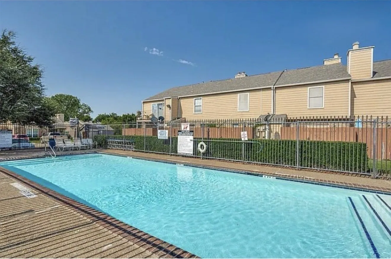 Rectangular swimming pool with integrated steps, surrounded by a metal fence and mature hedges