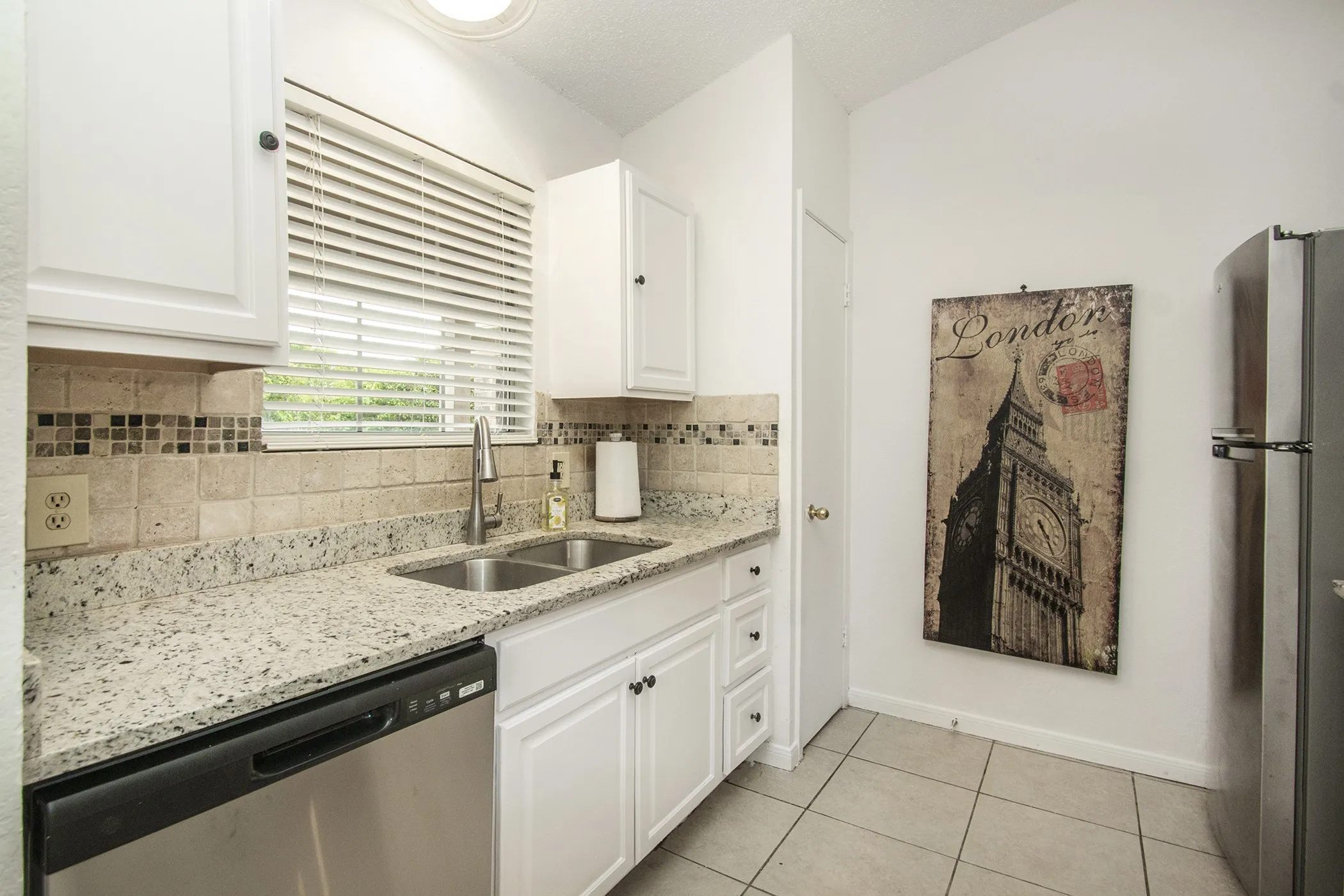 White cabinetry, stainless steel sink, tile backsplash with accent mosaic, granite-style countertops, and stainless steel dishwasher