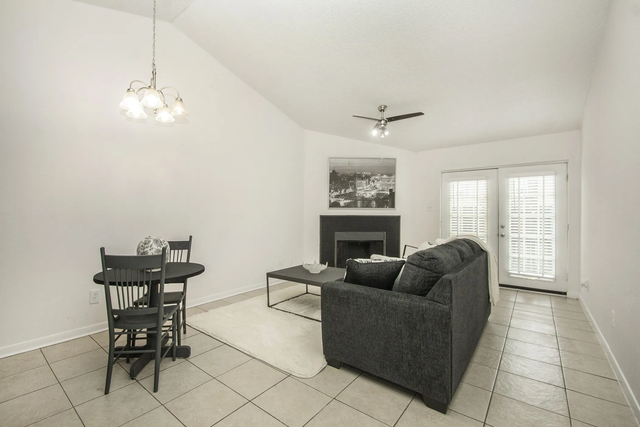 Vaulted ceiling with an attached chandelier and ceiling fan, tiled flooring, built-in fireplace, and double French doors