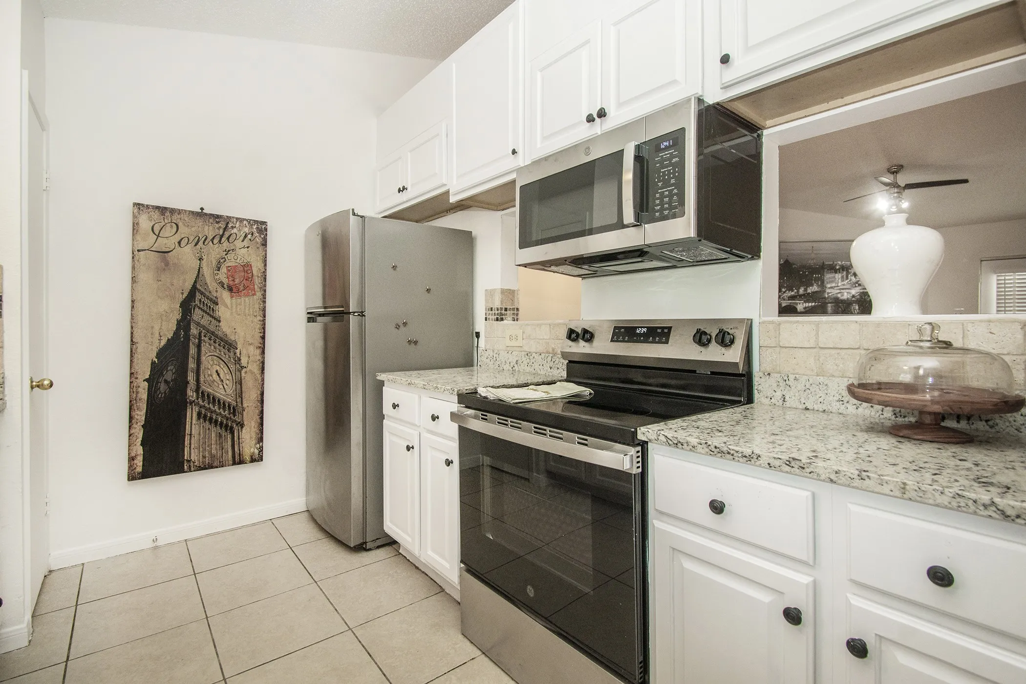 Recessed white cabinetry, stainless steel appliances, granite countertops, tile backsplash, and tile flooring