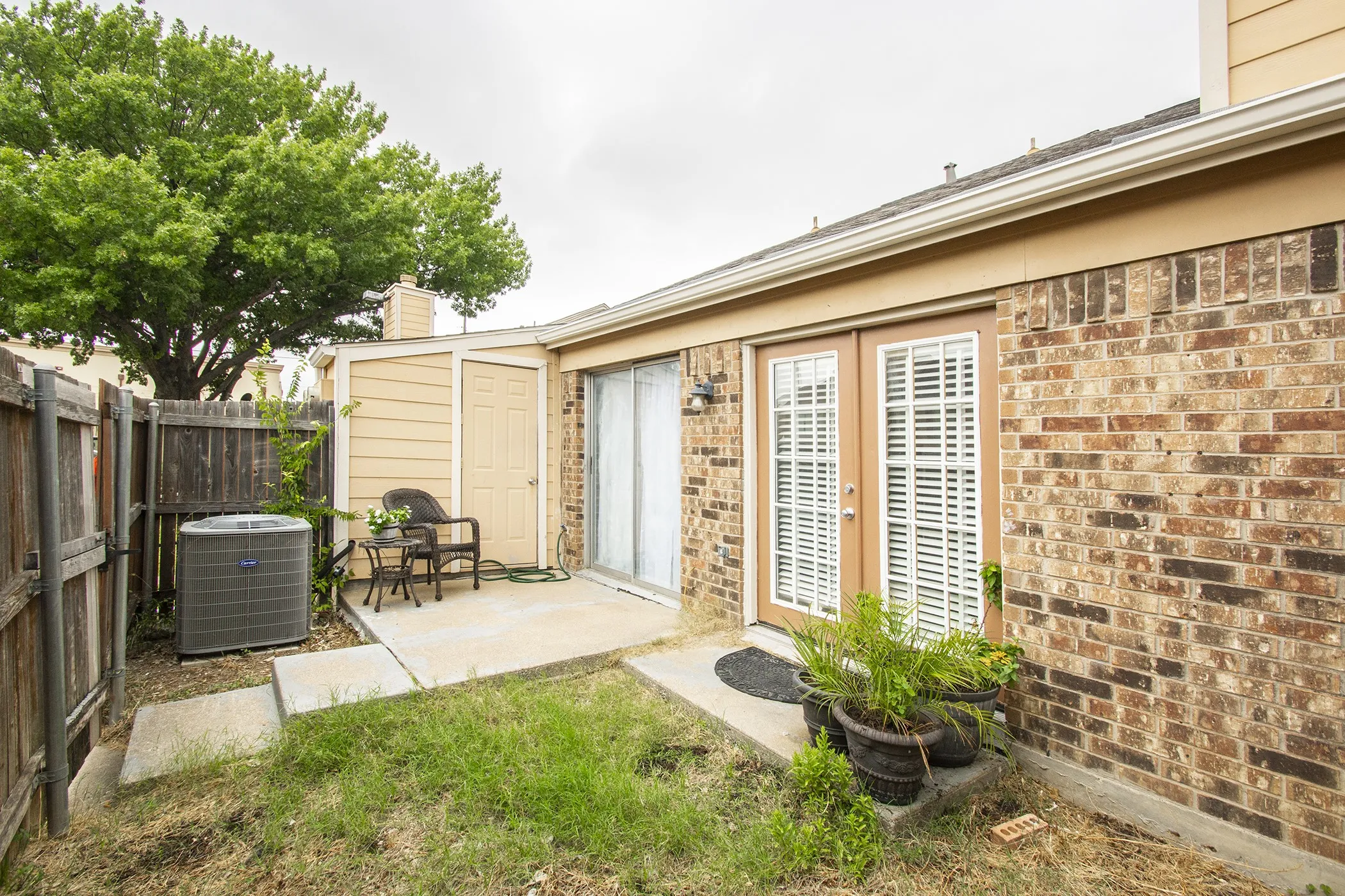 Private fenced patio with brick exterior, dual French doors, and an exterior storage unit