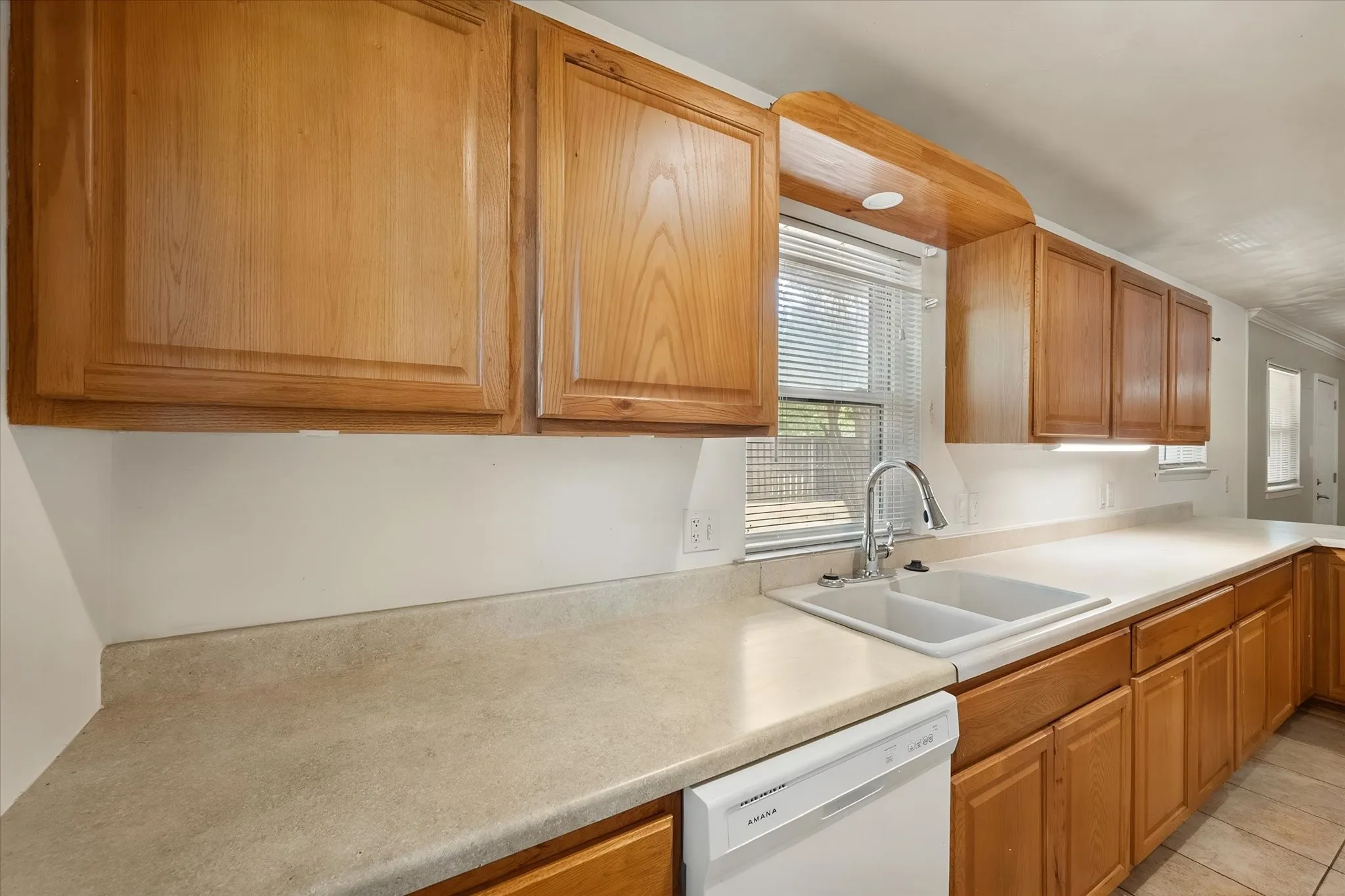 Kitchen featuring wood cabinetry, light-toned countertops, a double basin sink with a chrome faucet, under-cabinet lighting, and a built-in dishwasher