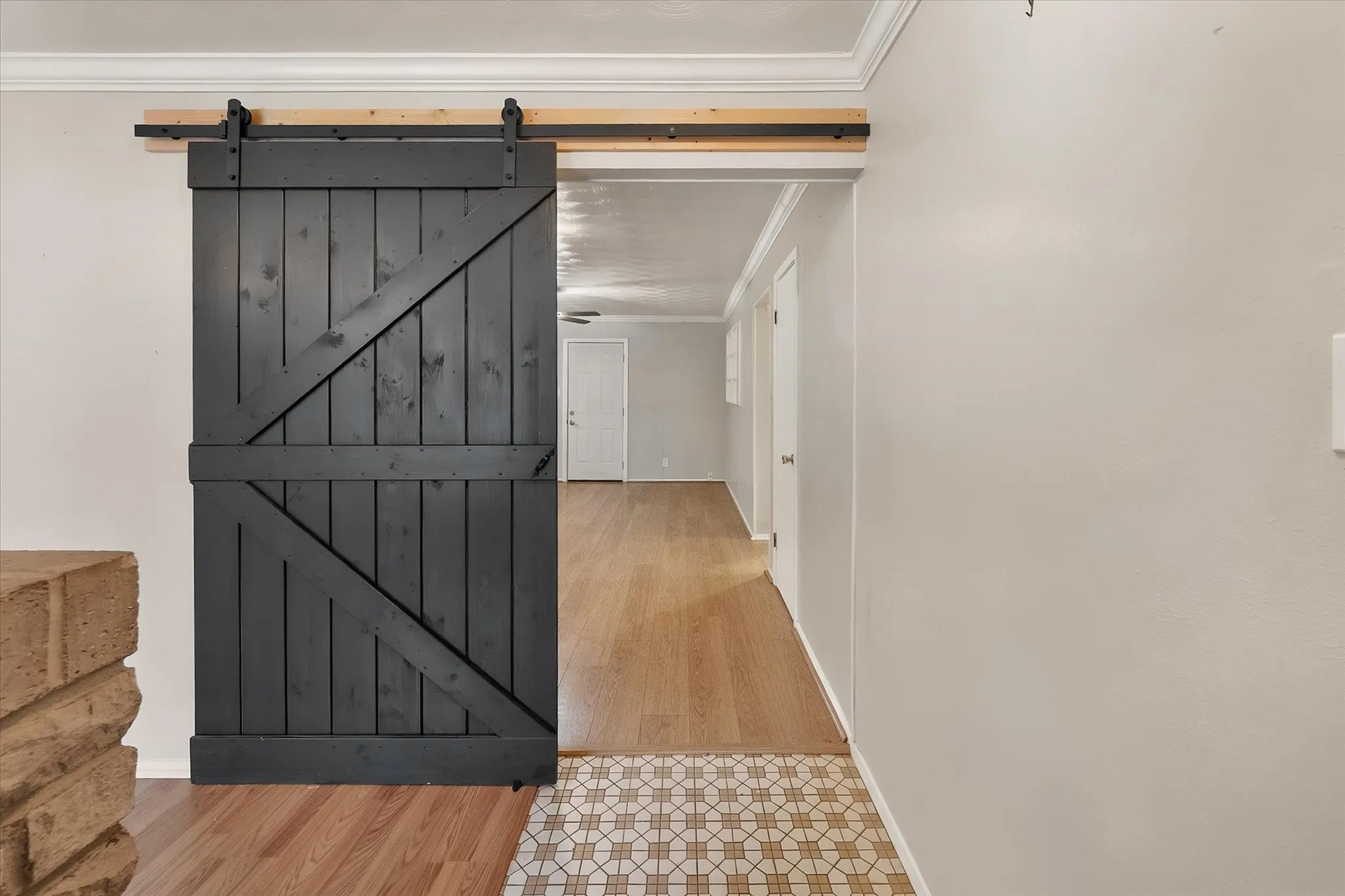 Black barn door with exposed rail hardware, wood-finish flooring, and crown molding