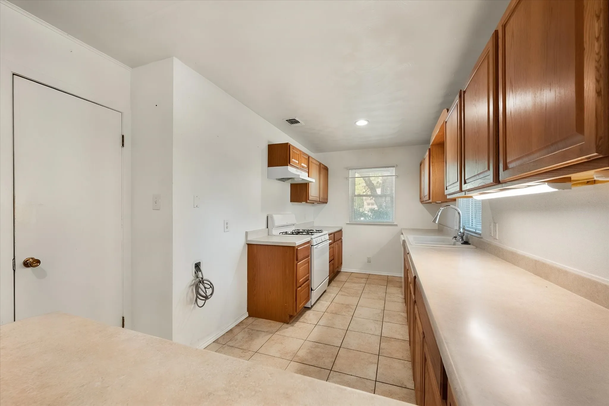 Kitchen featuring wood cabinetry, light-toned countertops, white appliances, and tiled flooring
