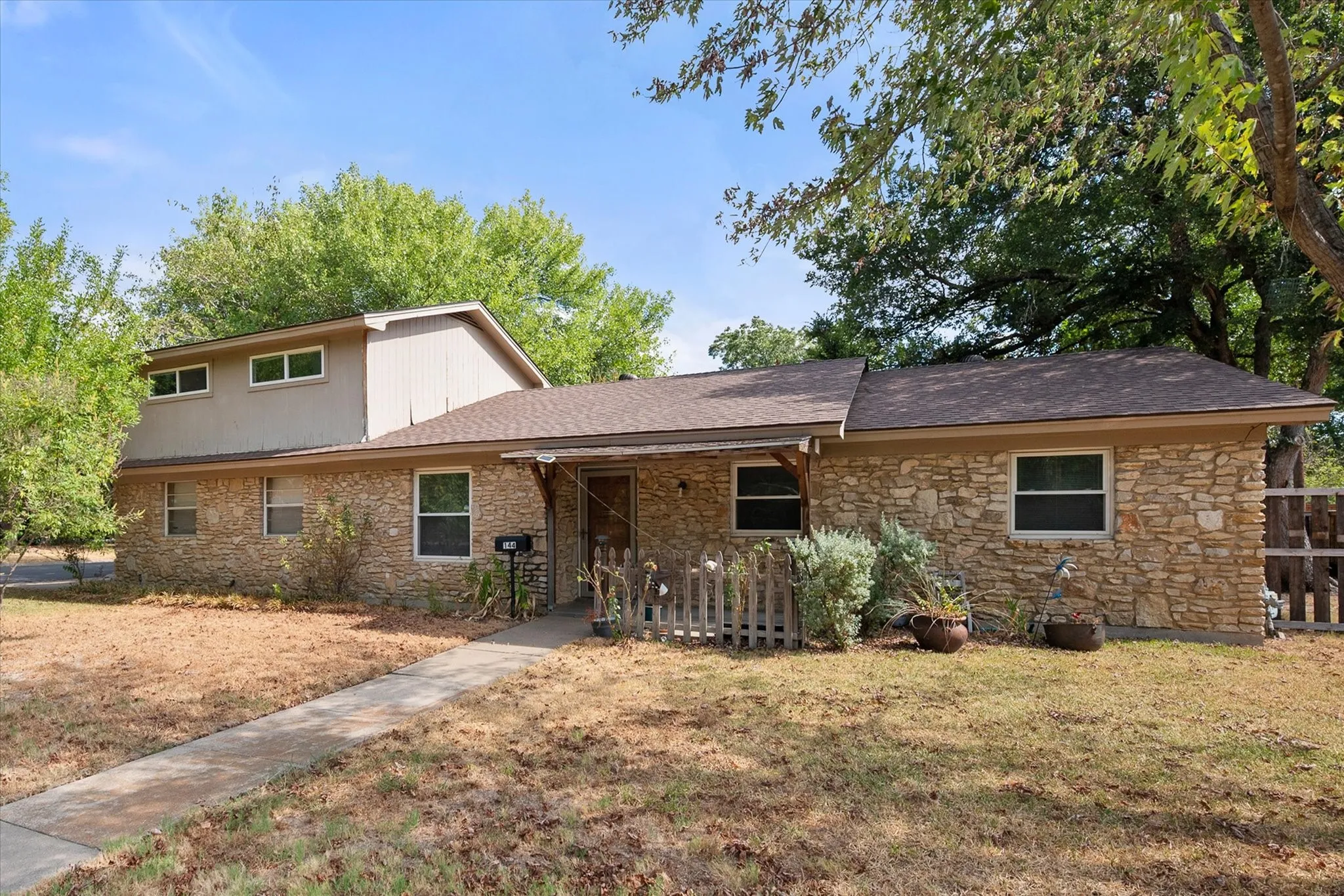 Stone exterior with a shingle roof and mature trees