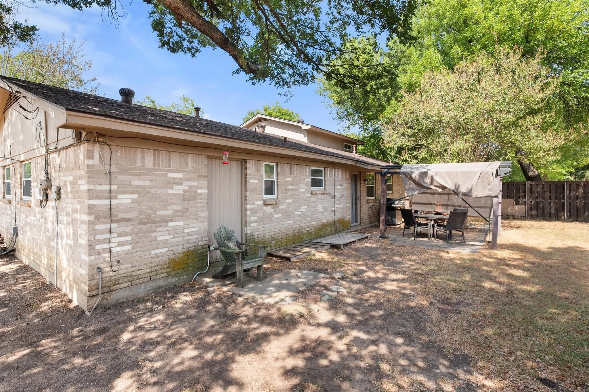 Brick exterior, multiple windows, covered patio area, partial privacy fencing, mature trees