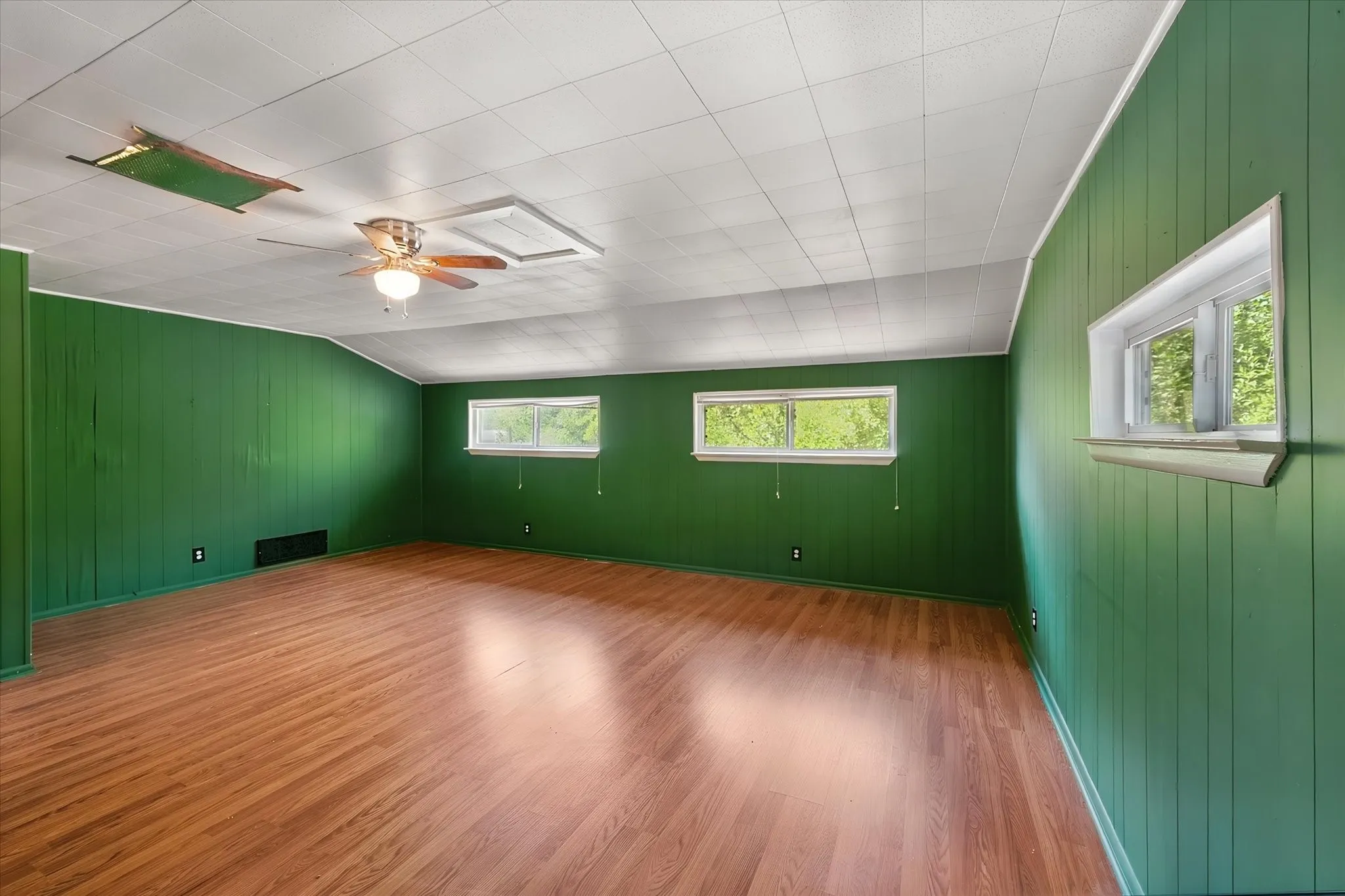 Wood-finish flooring, paneled walls, ceiling fan with integrated lighting, and multiple windows