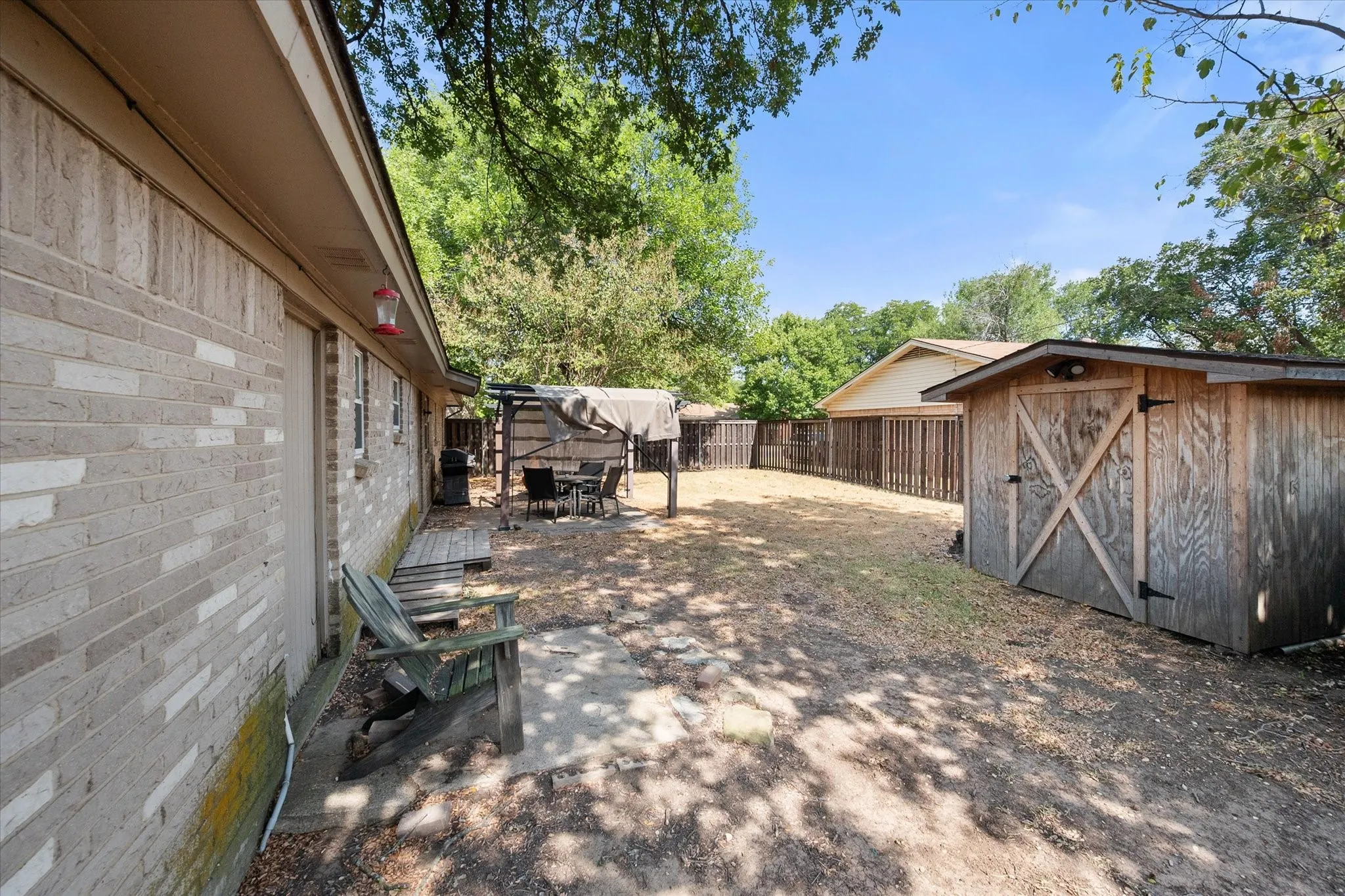 Expansive backyard featuring a wood storage shed, privacy fencing, and a covered outdoor patio area