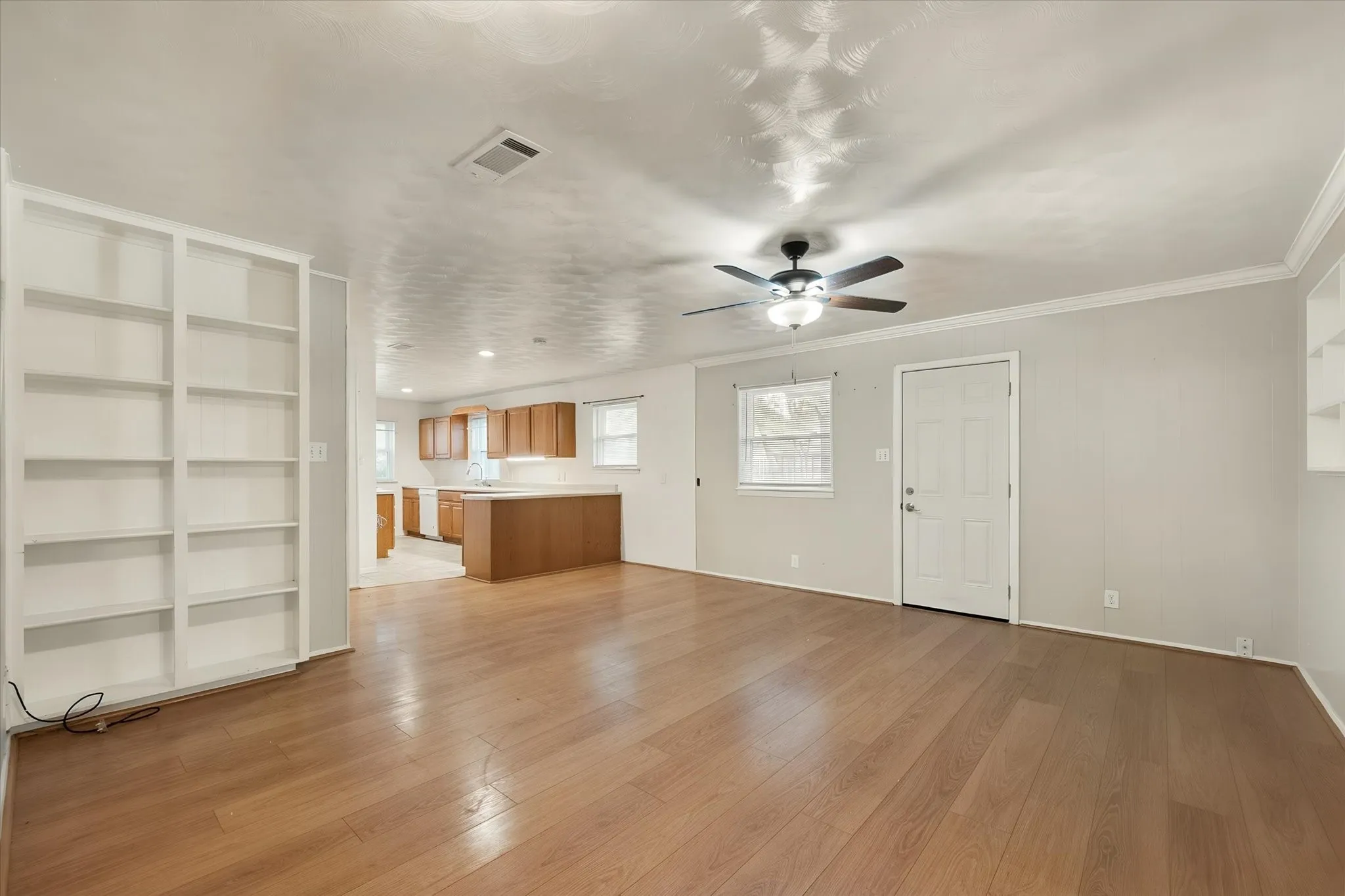 Open-concept living space featuring wood-finish flooring, built-in shelving, a ceiling fan, and crown molding