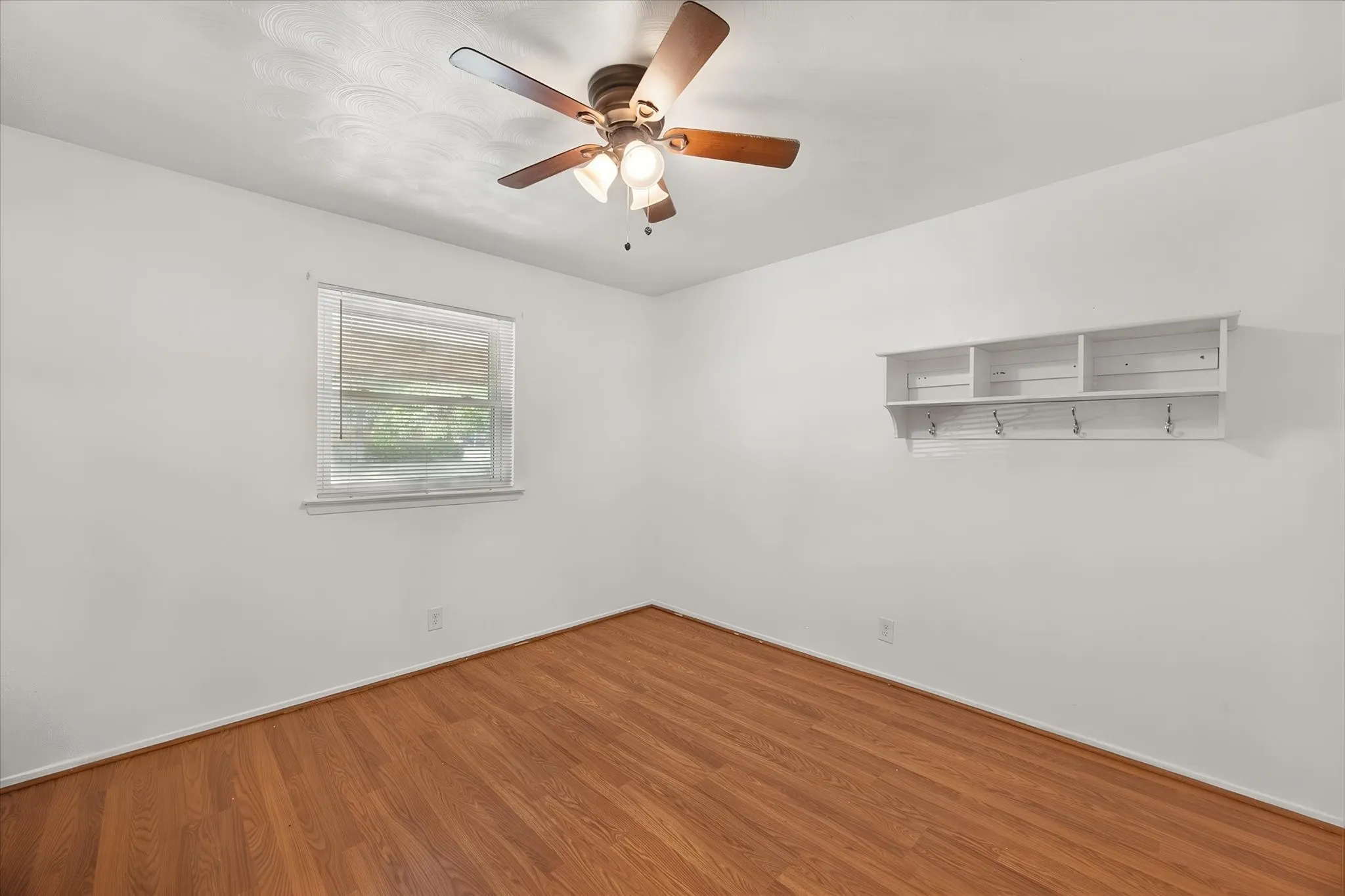 Wood-finish flooring throughout, white walls, built-in shelving with hooks, and a ceiling fan with light fixture