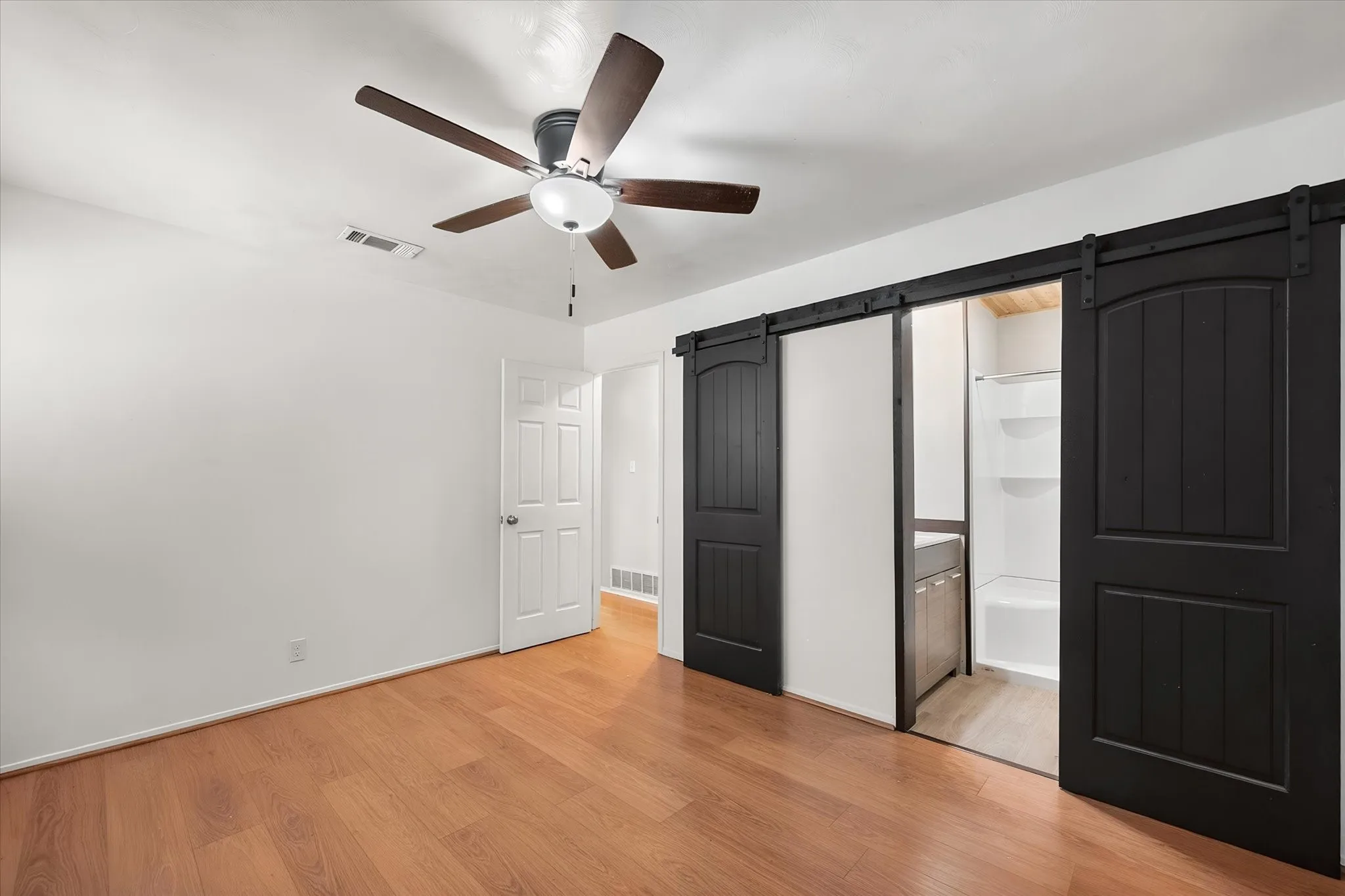 Wood-finish flooring, ceiling fan, white paneled door, and black barn doors