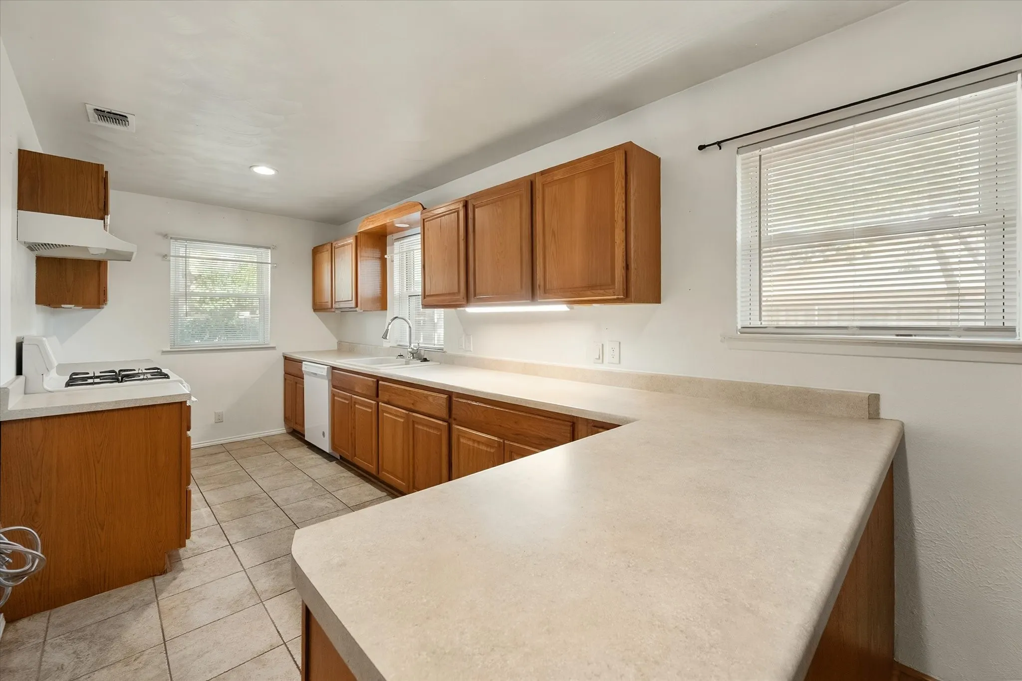 Kitchen featuring wood-finish cabinetry, solid surface countertops, a gas range, dishwasher, and tile flooring