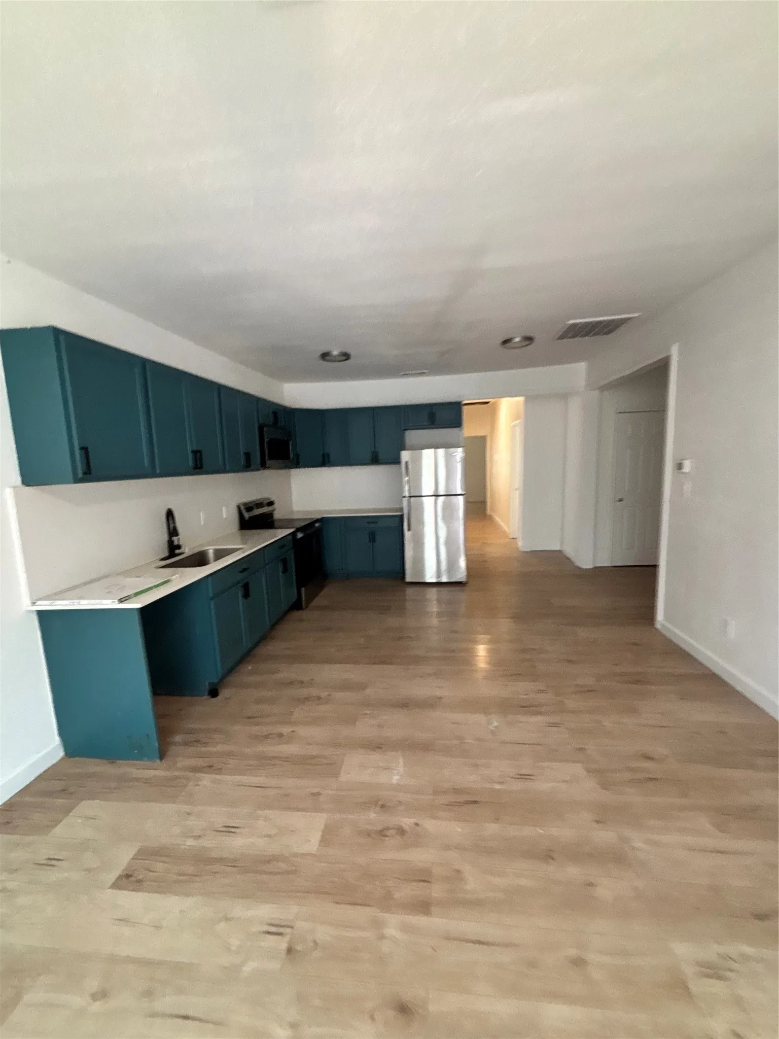 Kitchen featuring wood-finish flooring, teal cabinetry, and stainless steel appliances