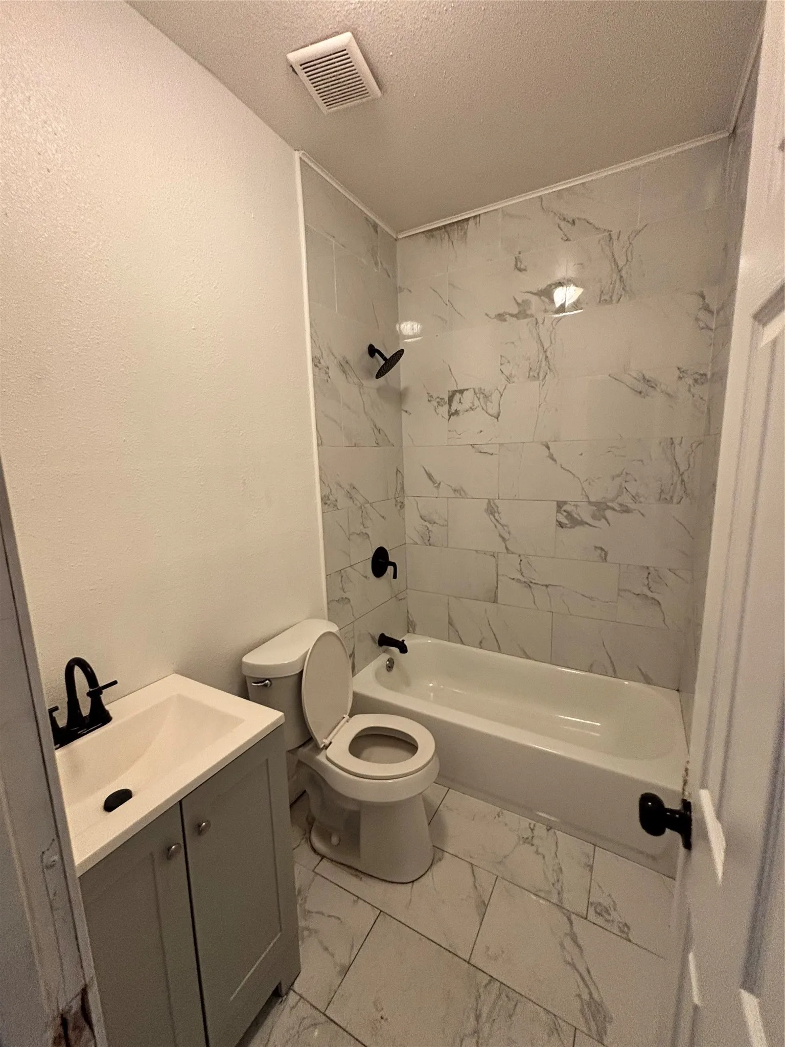Full bathroom featuring a single vanity with a white countertop, a toilet, a bathtub with a shower, and light-toned tile flooring