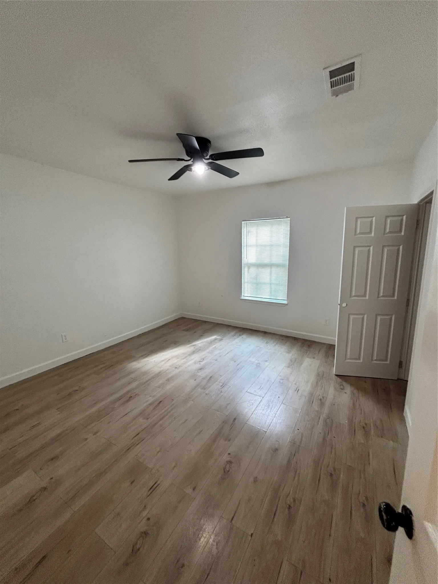 Wood-finish flooring, overhead ceiling fan with integrated lighting, white walls, and a multi-panel door