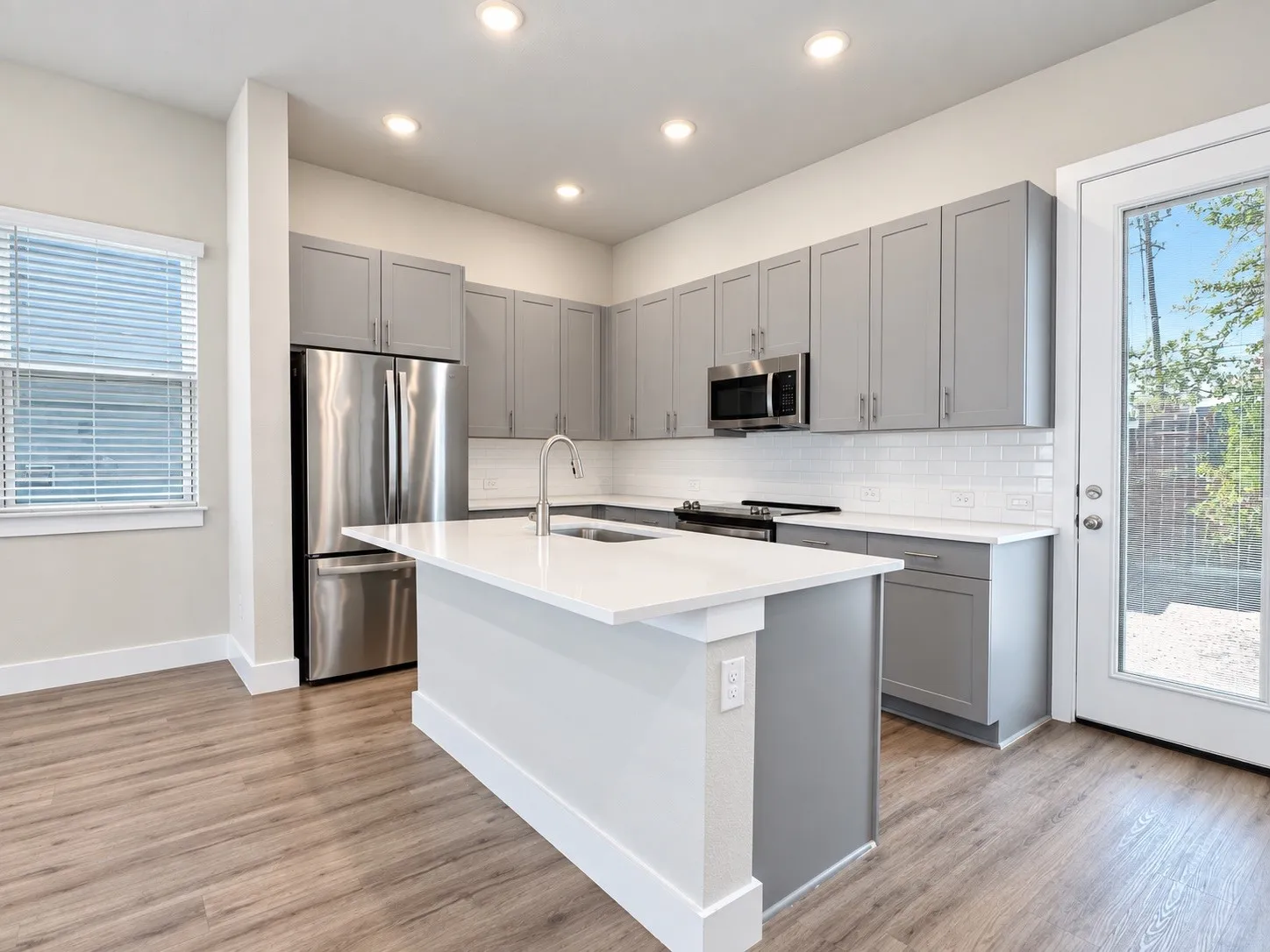 Kitchen featuring wood-finish flooring, recessed lighting, a center island with sink, stainless steel appliances, and a glass-paneled exterior door