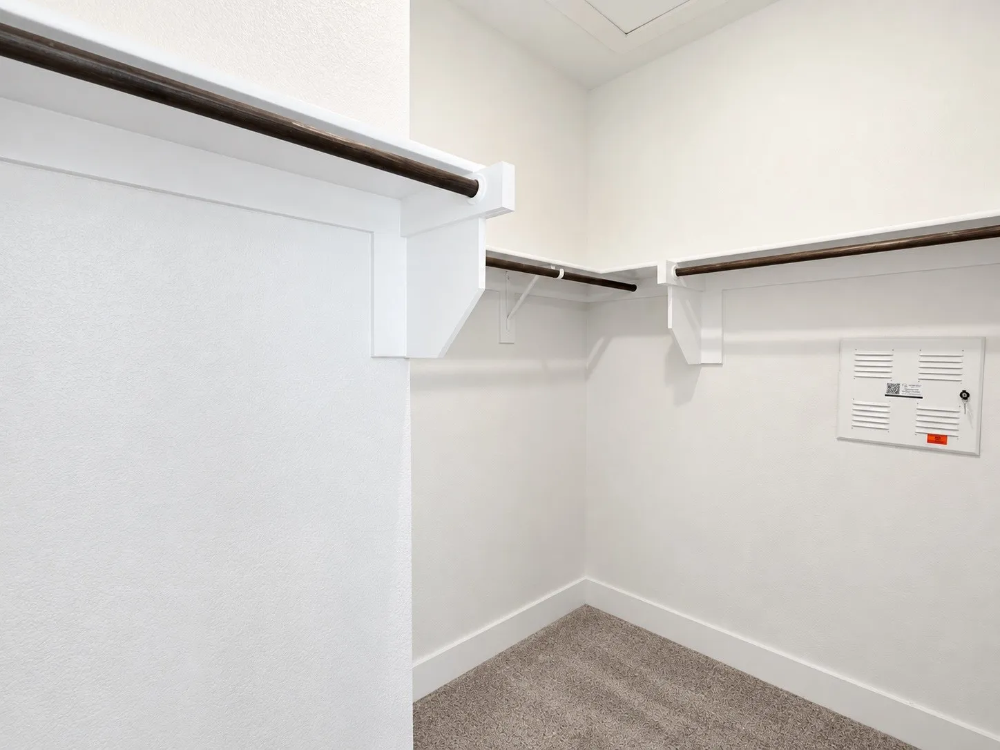 White walls with dark-finish hanging rods, white shelving, and a carpeted floor