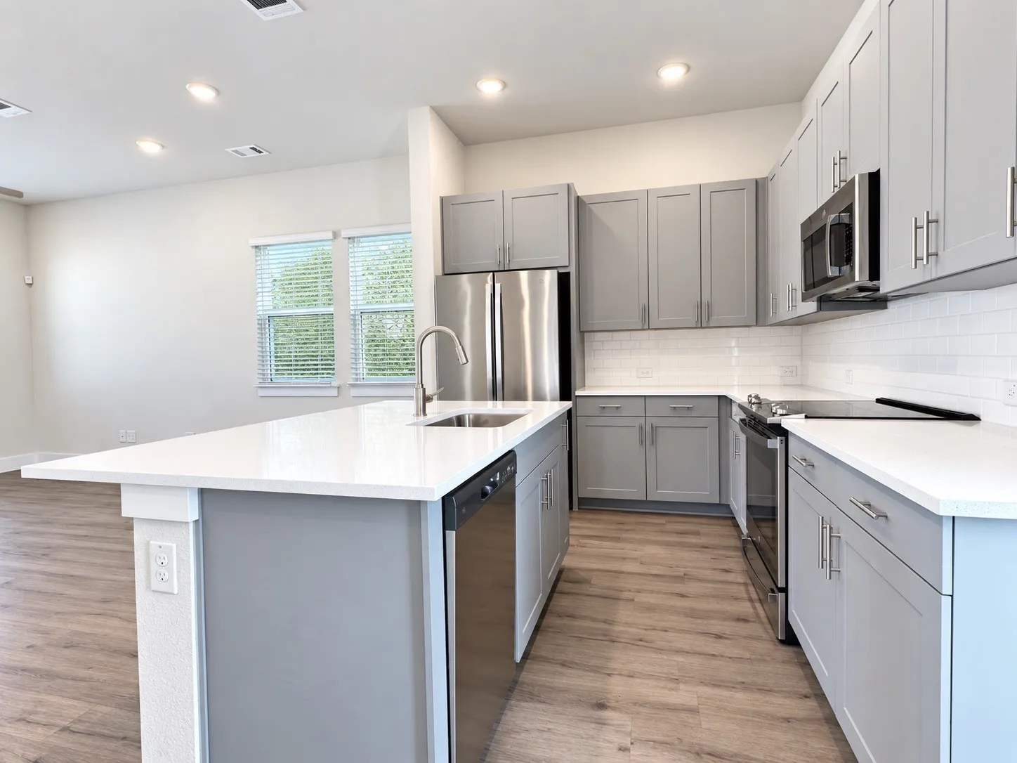 Kitchen featuring wood-finish flooring, white countertops, gray cabinetry, stainless steel appliances, and a tile backsplash